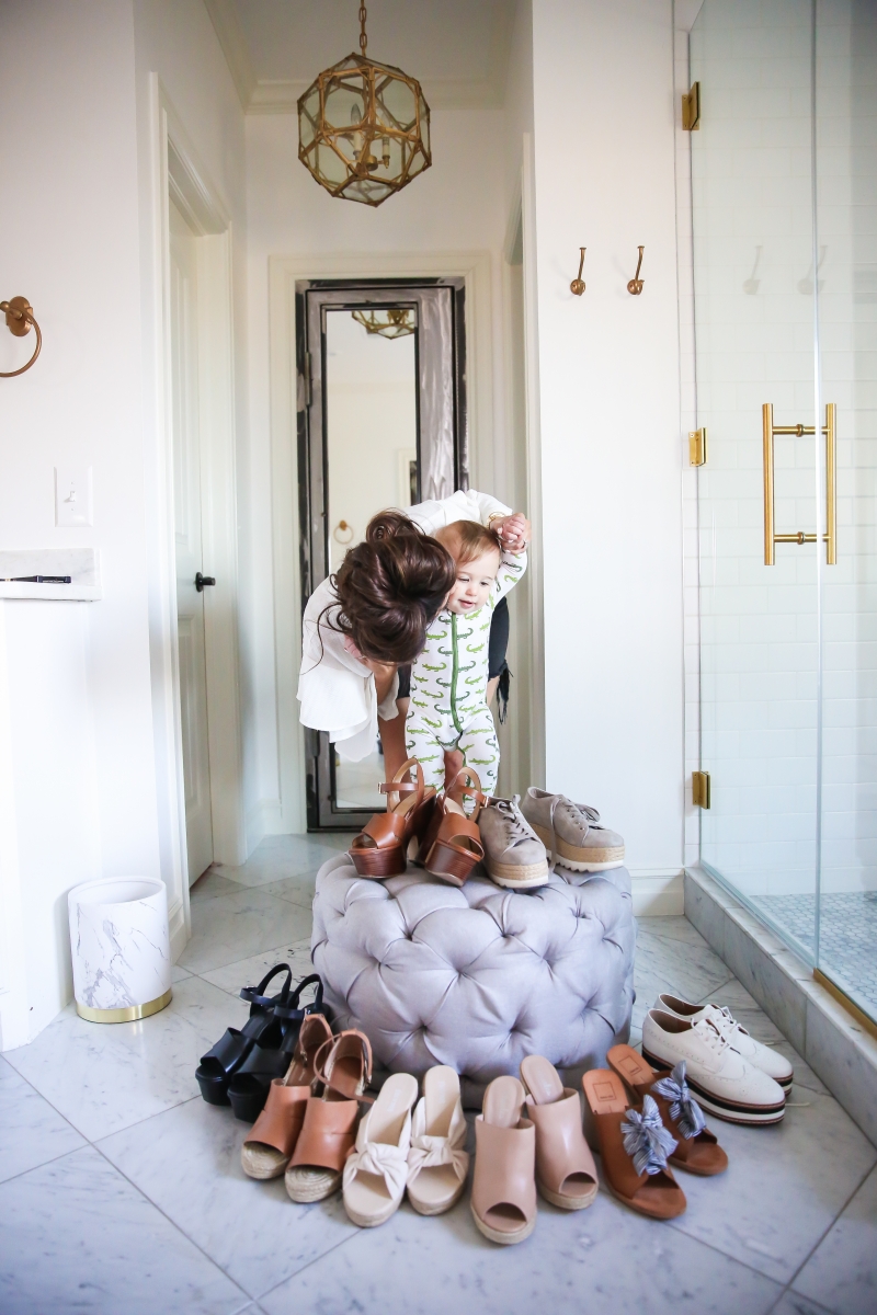 Cute Spring Shoes by popular US fashion blog, The Sweetest Thing: image of a mom holding her baby next to a display of cute spring shoes that are resting on or around a grey tufted ottoman. 