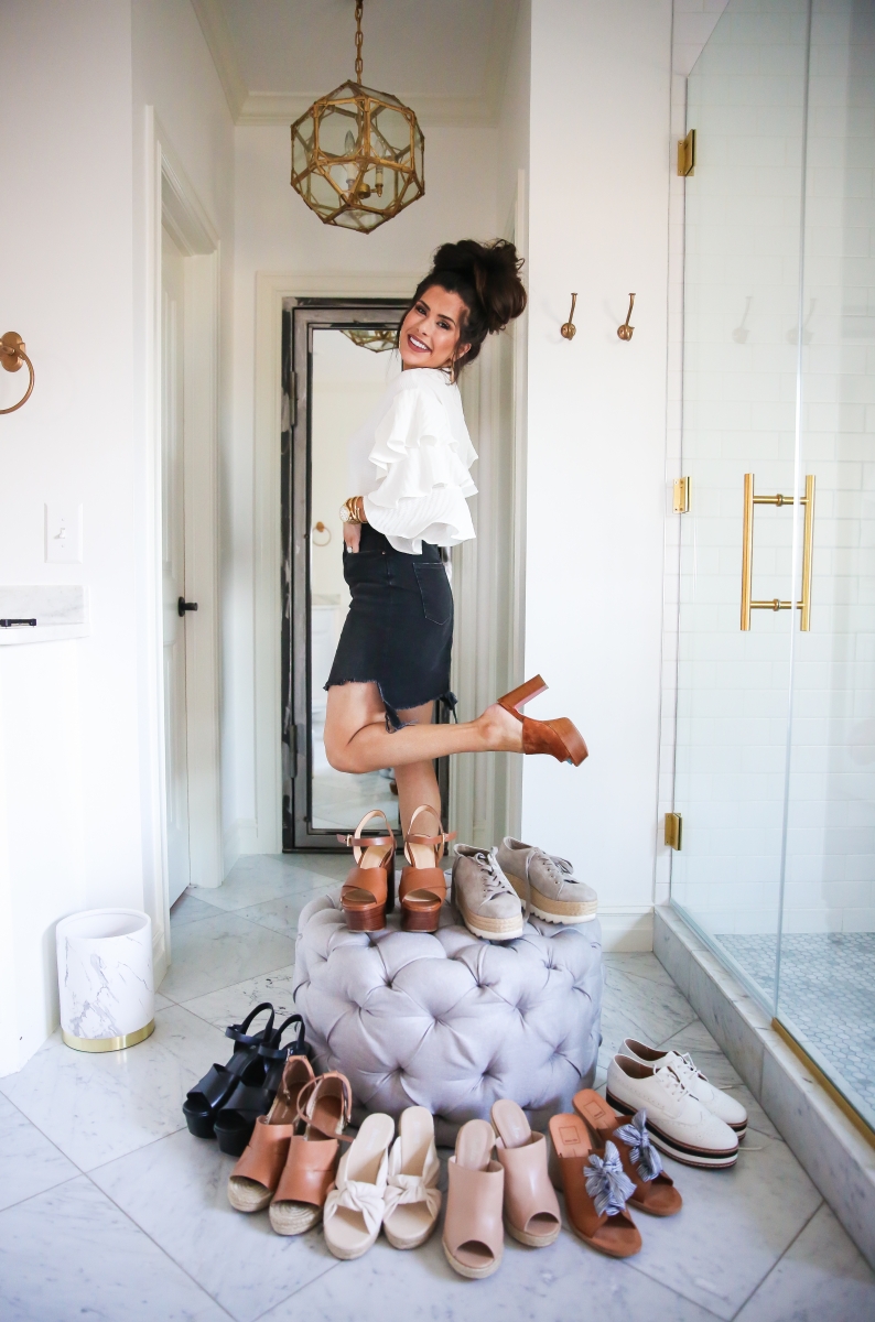 Cute Spring Shoes by popular US fashion blog, The Sweetest Thing: image of woman standing next to display of cute spring shoes on and around a grey tuft ottoman and wearing a white ruffle sleeve blouse and distressed black denim skirt. 