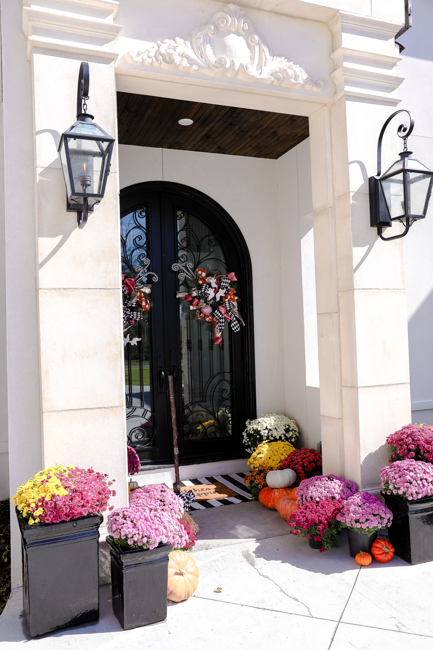 solar gas lights, luxury custom build home, pink mums, front door decor striped rug, pink mums, fall halloween decor, shop hello holidays, emily gemma | Fall & Halloween Home Decor Tour by popular Oklahoma life and style blog, The Sweetest Thing: image of the front entrance to a home decorated with pink mums, pumpkins, a black and white stripe rug, and a welcome mat.