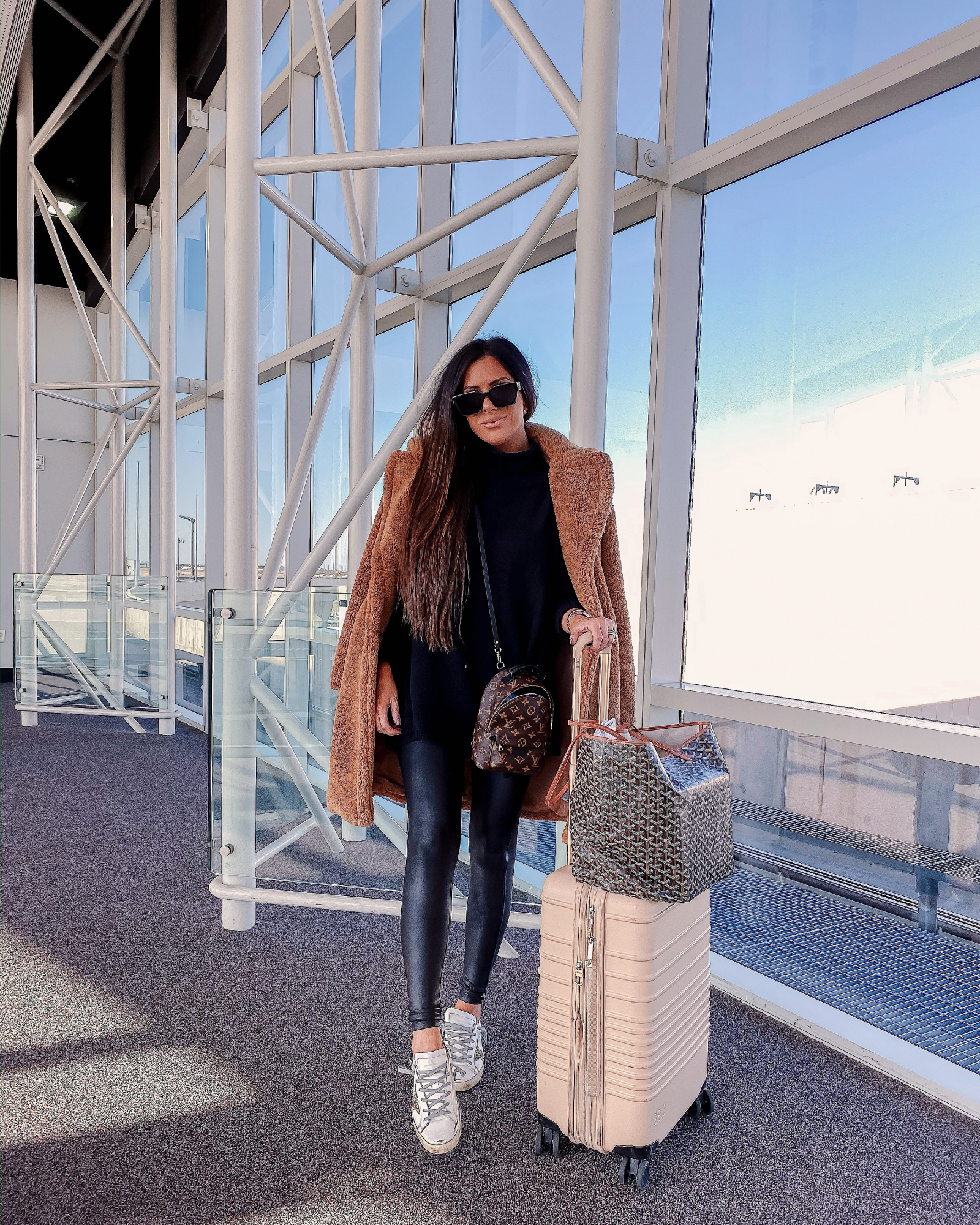 cute airport travel outfit idea, teddy coat outfit idea, goyard st louis, emily gemma | What to Wear on an Overnight Flight to Europe by popular Oklahoma fashion blog, The Sweetest Thing: image of a woman in an airport wearing a Free People Afterglow Mock Neck Sweater Dress, Spanx Faux Leather Leggings, GOLDEN GOOSE Superstar Low-Top Sneakers, Charlotte Tilbury Lip Cheat Lip Liner, Charlotte Tilbury Hot Lips Lipstick, Tom Ford Gloss Luxe Moisturizing Lipgloss, and Beis 21-Inch Rolling Spinner Suitcase. 