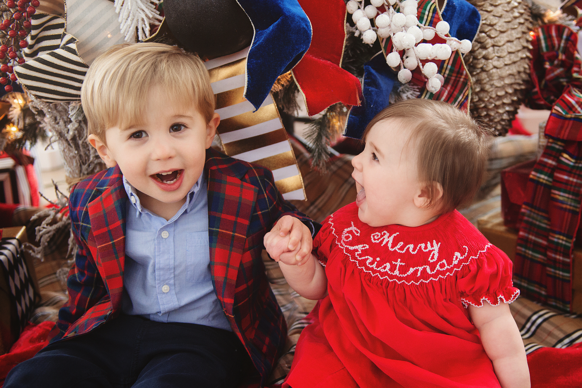 family Christmas card outfit inspiration, smocked Christmas dress baby, baby boy fashion Christmas, pinterest Christmas tree decor, shop hello holidays, Emily Gemma, the sweetest thing blog | Merry Christmas Wishes To You & Yours🎁❤️🎄 [Our Christmas Card 2019] by popular Oklahoma life and style blog, The Sweetest Thing: image a brother and sister sitting in front of their Christmas tree and wearing Smocked Auctions MERRY CHRISTMAS SMOCKED BISHOP RED CORDUROY dress, Zara BASIC SERGED SKINNY JEANS, Zara  LEATHER LOAFERS, Janie and Jack POPLIN SHIRT, Janie and Jack PLAID WOOL BLAZER. 