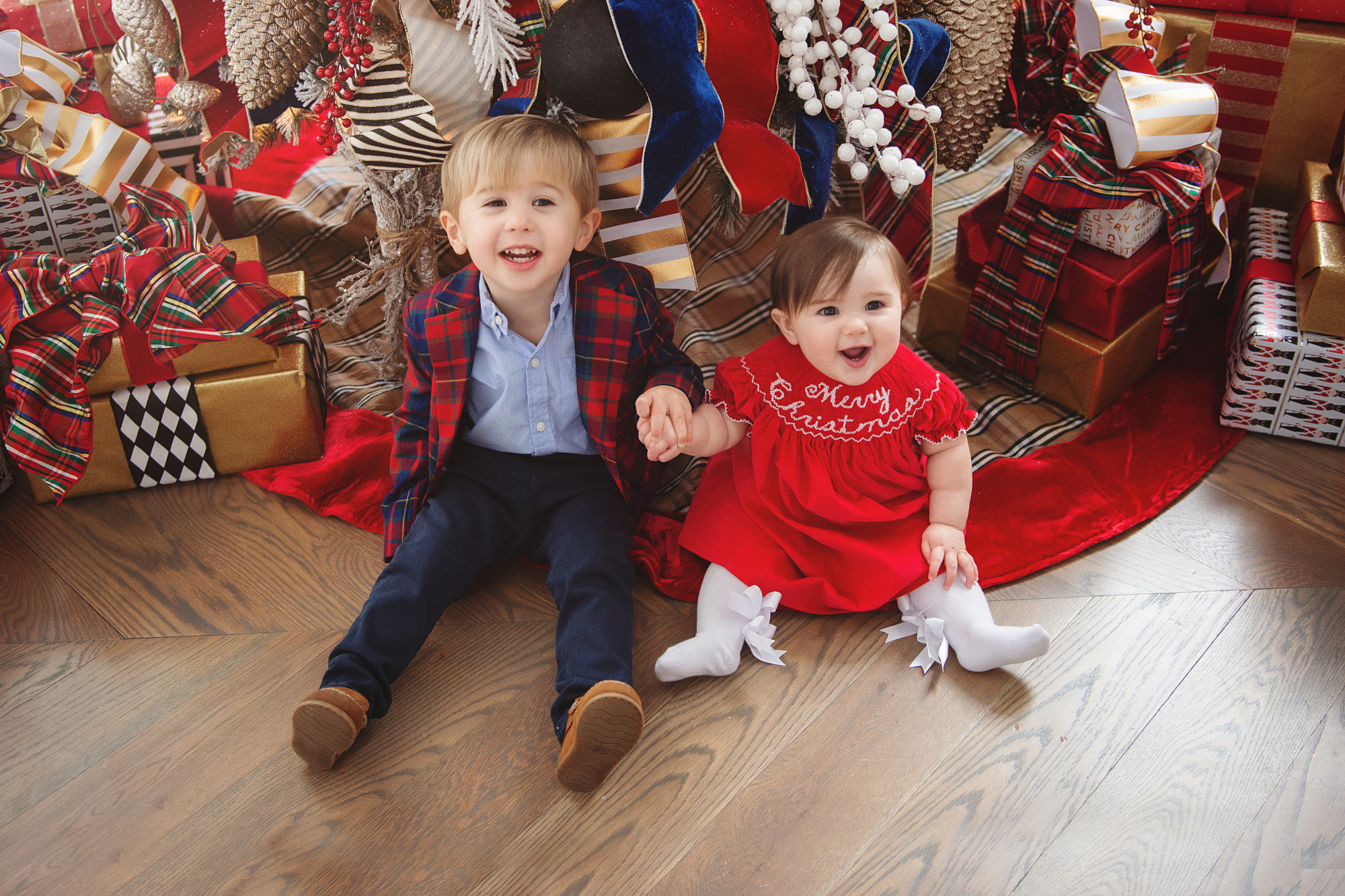 family Christmas card outfit inspiration, smocked Christmas dress baby, baby boy fashion Christmas, pinterest Christmas tree decor, shop hello holidays, Emily Gemma, the sweetest thing blog | Merry Christmas Wishes To You & Yours🎁❤️🎄 [Our Christmas Card 2019] by popular Oklahoma life and style blog, The Sweetest Thing: image a brother and sister sitting in front of their Christmas tree and wearing Smocked Auctions MERRY CHRISTMAS SMOCKED BISHOP RED CORDUROY dress, Zara BASIC SERGED SKINNY JEANS, Zara  LEATHER LOAFERS, Janie and Jack POPLIN SHIRT, Janie and Jack PLAID WOOL BLAZER. 