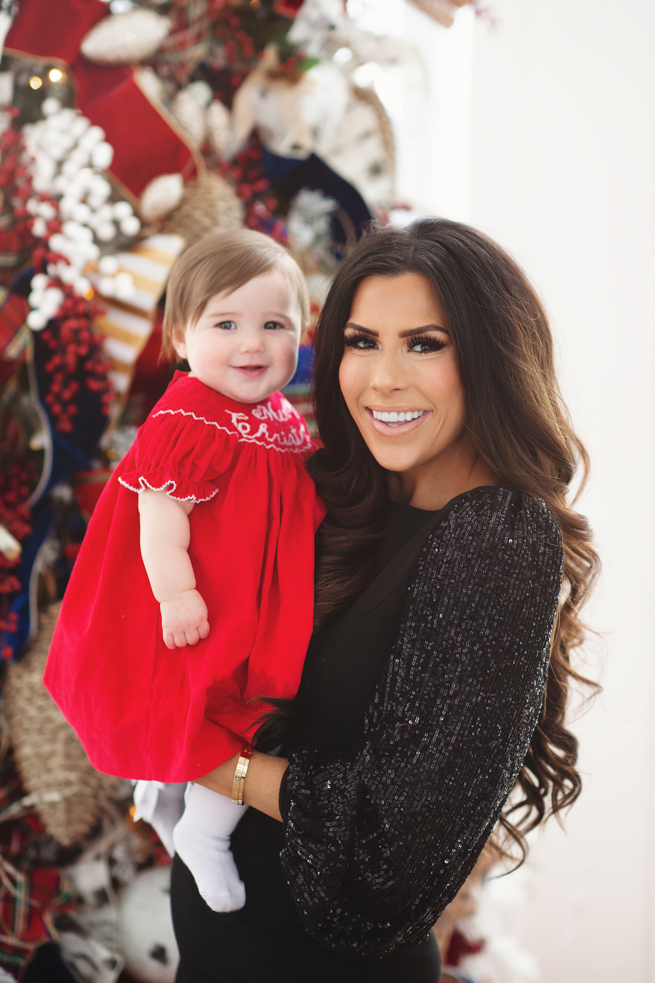 family Christmas card outfit inspiration, smocked Christmas dress baby, baby boy fashion Christmas, pinterest Christmas tree decor, shop hello holidays, Emily Gemma, the sweetest thing blog | Merry Christmas Wishes To You & Yours🎁❤️🎄 [Our Christmas Card 2019] by popular Oklahoma life and style blog, The Sweetest Thing: image a mom holding her baby daughter in front of their Christmas tree and wearing Smocked Auctions MERRY CHRISTMAS SMOCKED BISHOP RED CORDUROY dress, CHRISTIAN LOUBOUTIN So Kate 120 suede pumps, and Nordstrom Eliza J Long Sequin Sleeve Sheath Dress.