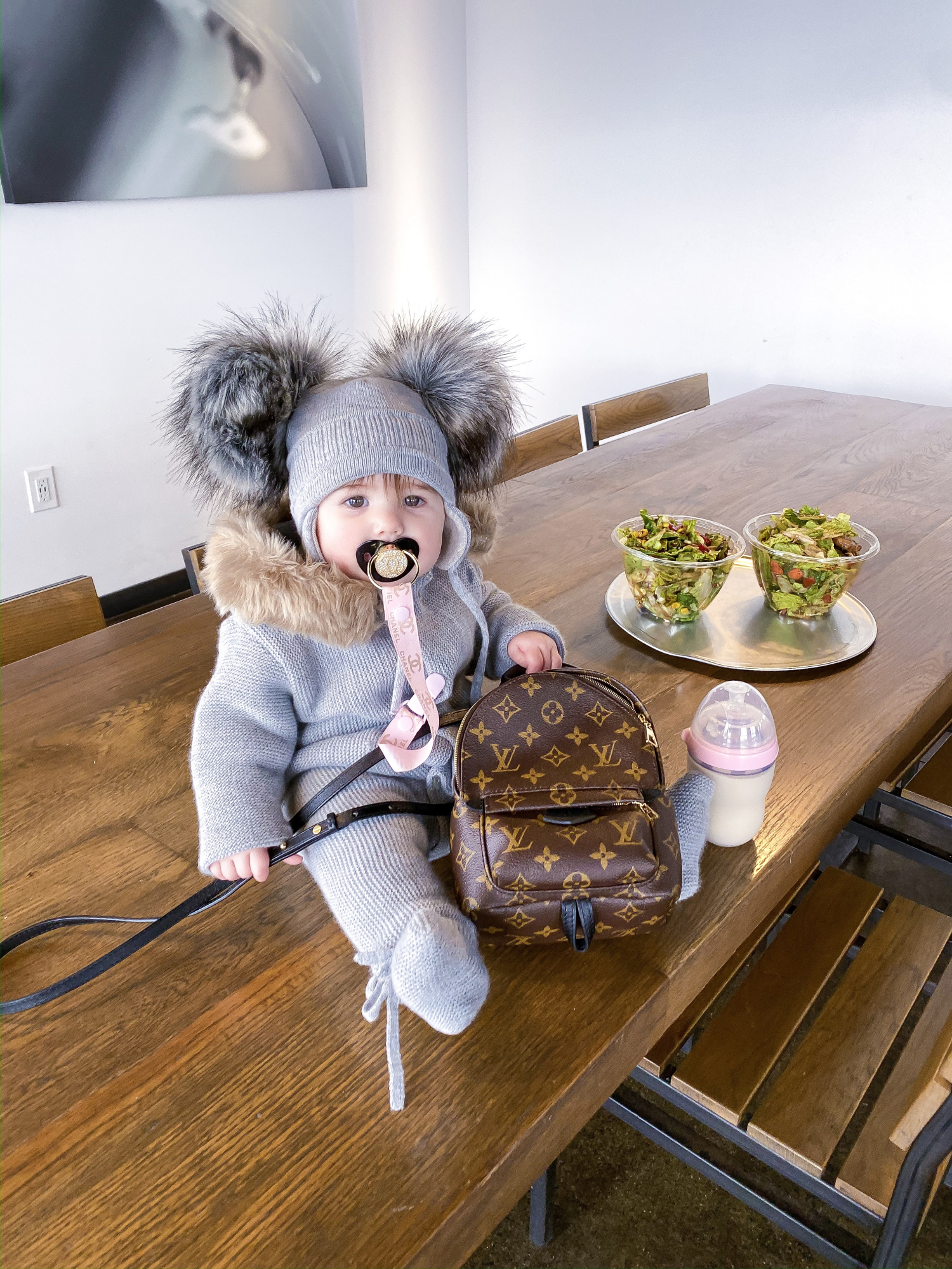 baby girl fashion pinterest, louis vuitton palm springs backpack | A YEAR IN REVIEW : MASSIVE 2019 INSTAGRAM RECAP by popular Oklahoma life and style blog, The Sweetest Thing: image of a baby sitting on a table next to some salad bowls and wearing a grey double pom-pom hat and holding a Louis Vuitton mini backpack. 