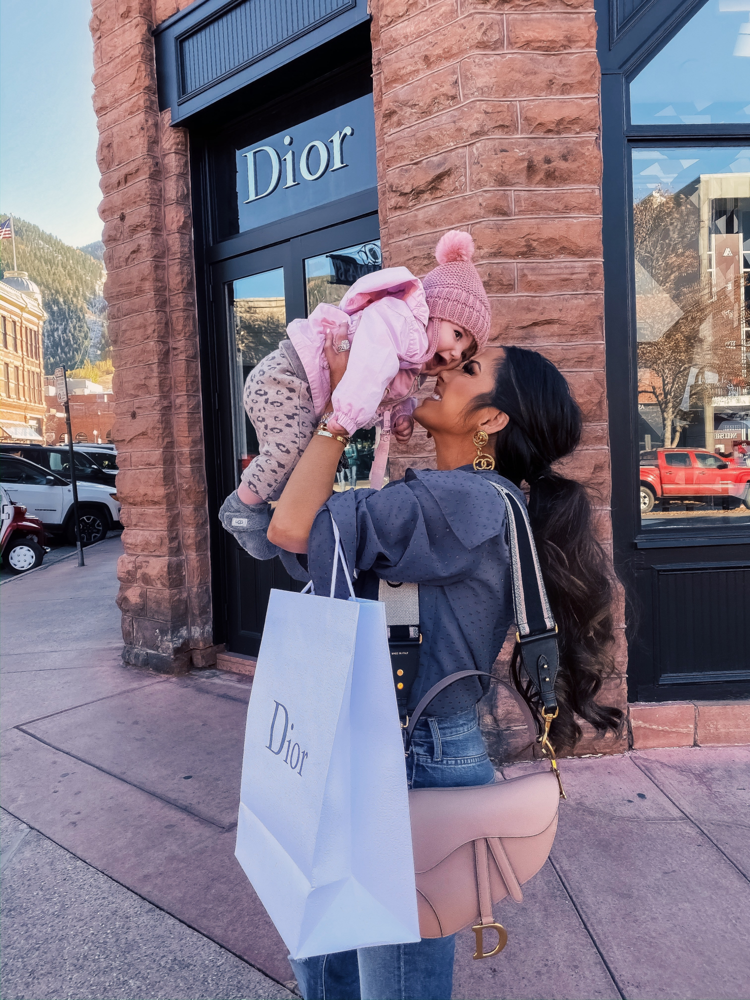baby girl fashionista, dior in aspen, dior nude saddle bag, emily gemma | A YEAR IN REVIEW : MASSIVE 2019 INSTAGRAM RECAP by popular Oklahoma life and style blog, The Sweetest Thing: image of a woman holding her baby outside a Dior store in Aspen, Colorado and wearing Chanel earrings, Nordstrom Tie Neck Dobby Blouse TOPSHOP, and Nordstrom The Tripper High Waist Crop Bootcut Jeans MOTHER.