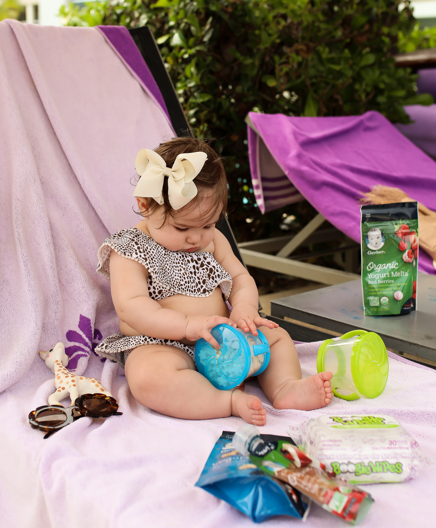 Christmas In Cancun🌟🎄🎁 [+ A Few Baby Travel Must-Haves] by popular Oklahoma travel blog, The Sweetest Thing: image of a baby in Cancun, Mexico holding a Walmart Munchkin Snack Catcher Snack Cup with Gerber Puff cereal snack inside, with a bottle resting on her high chair tray and some Boogie wipes and Gerber Organic Yogurt melts next to her.