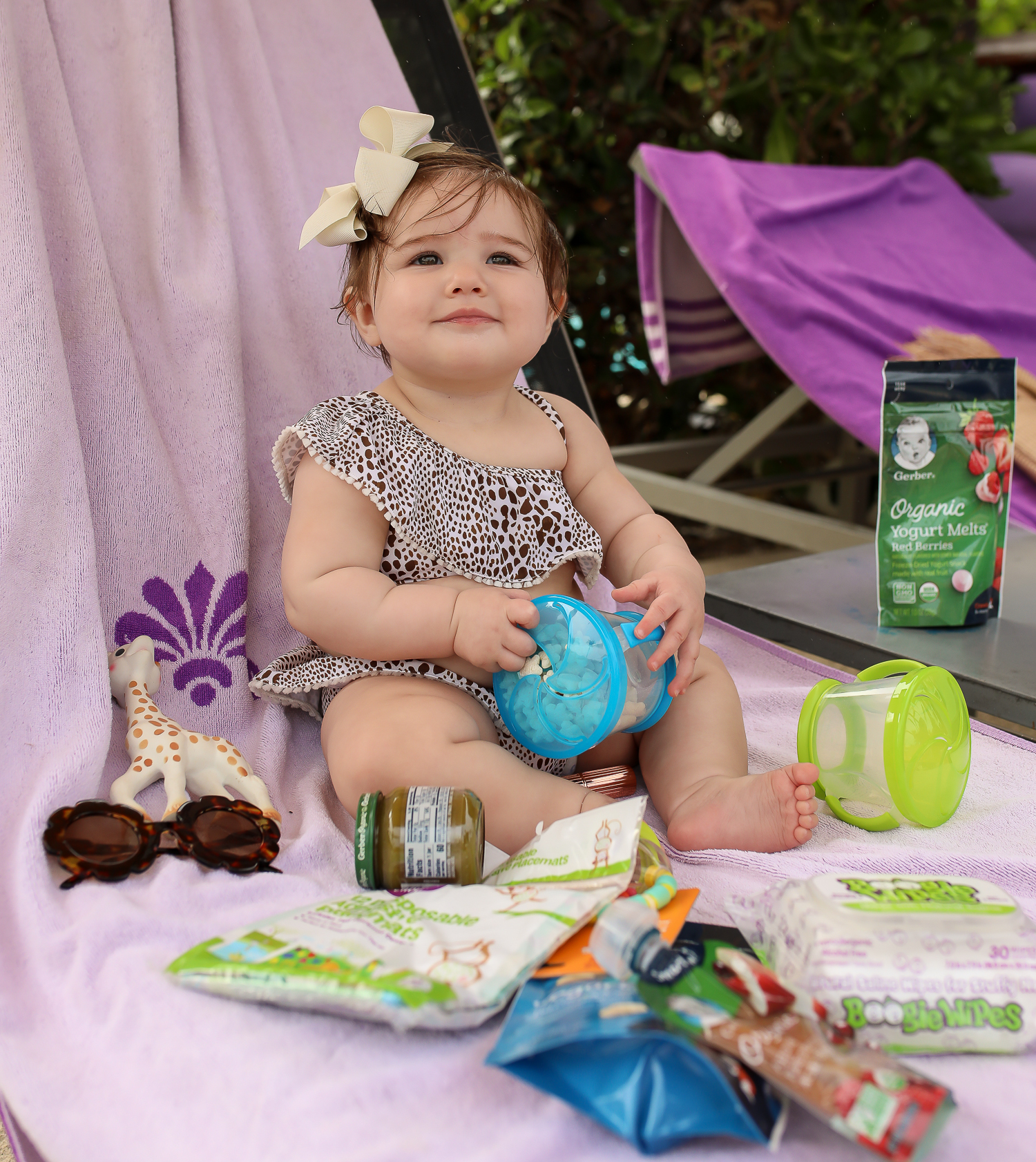 Christmas In Cancun🌟🎄🎁 [+ A Few Baby Travel Must-Haves] by popular Oklahoma travel blog, The Sweetest Thing: image of a baby in Cancun, Mexico holding a Walmart Munchkin Snack Catcher Snack Cup with Gerber Puff cereal snack inside, with a bottle resting on her high chair tray and some Boogie wipes and Gerber Organic Yogurt melts next to her high chair. 