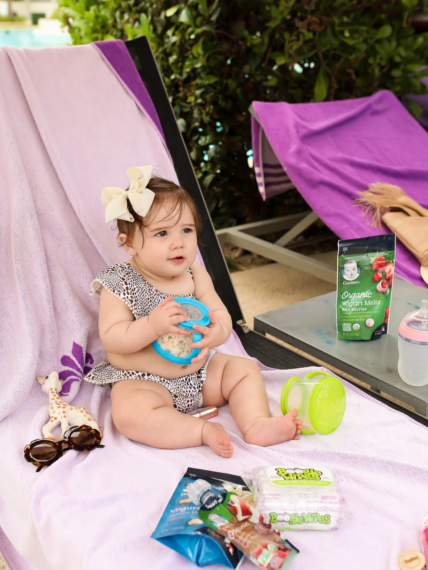 Christmas In Cancun🌟🎄🎁 [+ A Few Baby Travel Must-Haves] by popular Oklahoma travel blog, The Sweetest Thing: image of a baby in Cancun, Mexico holding a Walmart Munchkin Snack Catcher Snack Cup with Gerber Puff cereal snack inside, with a bottle resting on her high chair tray and some Boogie wipes and Gerber Organic Yogurt melts next to her.