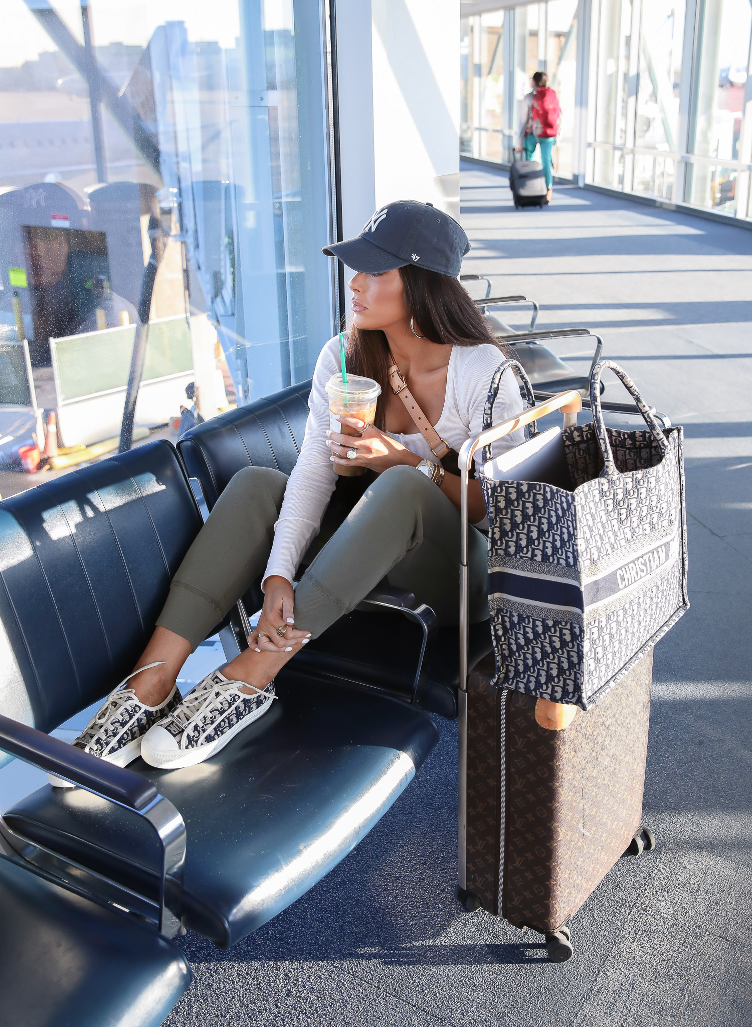 airport outfit idea, cute airport fashion outfit, dior sneakers womens 2020, pinterest airport fashion, horizon louis vuitton carryon, dior oblique tote, emily gemma-2 | Airport Style by popular US life and style blog, The Sweetest Thing: image of a woman in an airport wearing a Abercrombie Long-Sleeve Cozy Henley, Abercrombie High Rise Joggers, Dior WALK'N'DIOR SNEAKER IN OBLIQUE EMBROIDERED CANVAS, Nordstrom 21-Inch Rolling Spinner Suitcase, Nordstrom Demonbreun Hoop Earrings UNCOMMON JAMES BY KRISTIN CAVALLARI, Nordstrom Lip Cheat Lip Liner CHARLOTTE TILBURY, Nordstrom Hot Lips Lipstick CHARLOTTE TILBURY, Nordstrom Gloss Luxe Moisturizing Lipgloss TOM FORD, and Urban Outfitters MLB Baseball Hat.