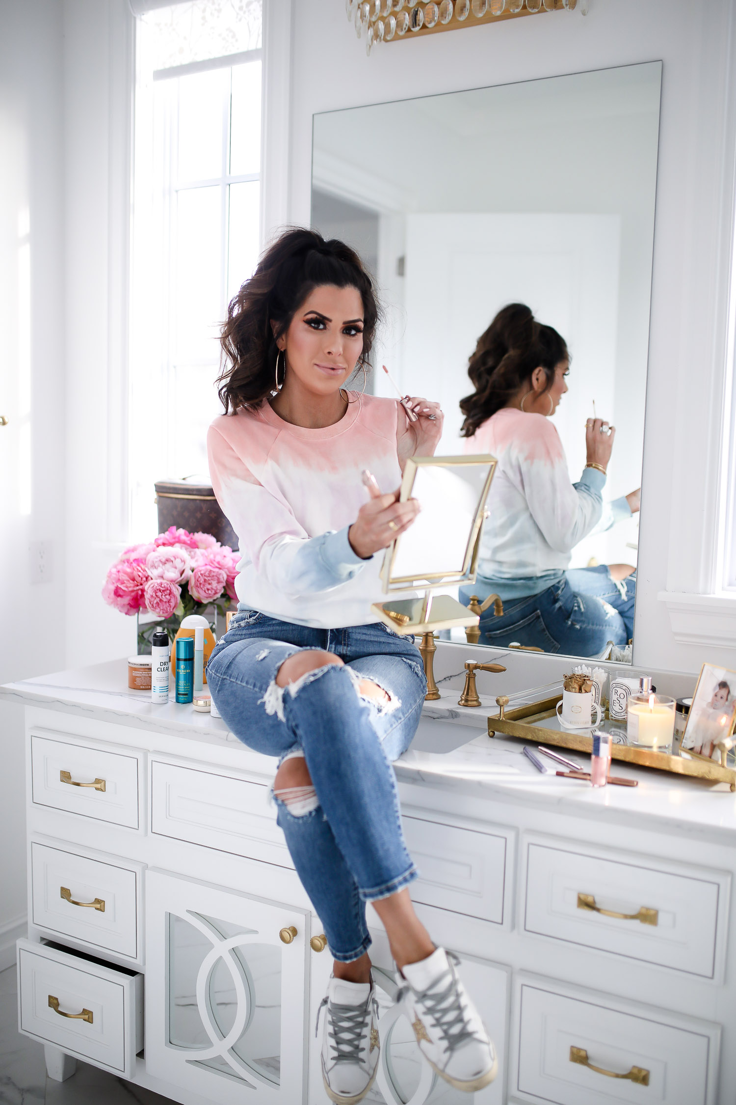 Sephora Favorites by popular US beauty blog, The Sweetest Thing: image of a woman sitting on her bathroom counter and holding a lip gloss applicator and handheld mirror. 
