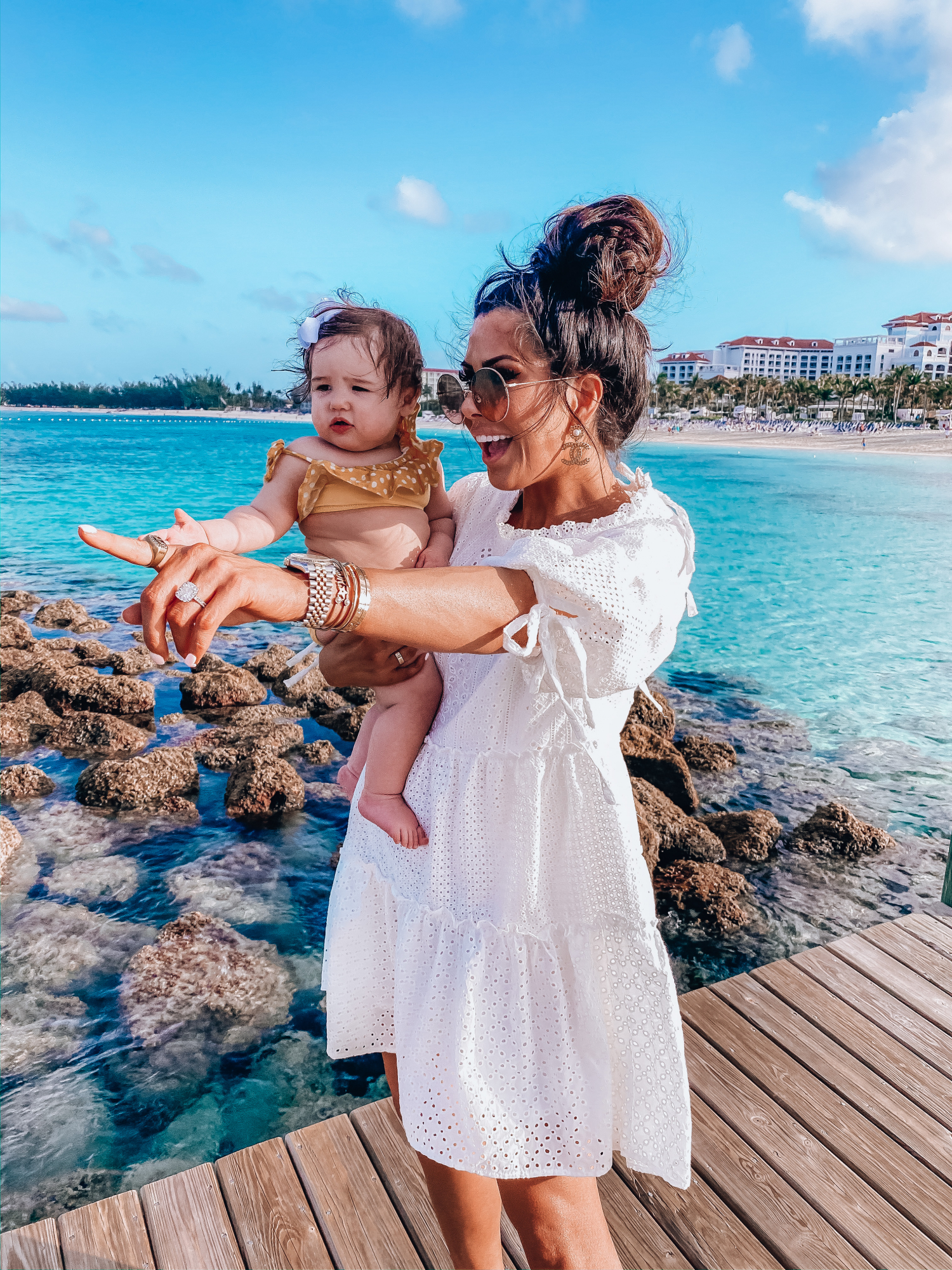 baby girl fashionista swimsuit, emily gemma | What to Wear in the Bahamas by popular US travel blog, The Sweetest Thing: image of a woman holding her baby girl and wearing a Red Dress On That Note White Eyelet Dress, CULT GAIA Banu Twisted Raffia Clutch, Dior DiorSociety2 Round Beaded Metal Sunglasses, Steve Madden TRAVEL CLEAR, Nordstrom Pillow Talk Lip Cheat Lip Liner CHARLOTTE TILBURY, Nordstrom Hot Lips Lipstick CHARLOTTE TILBURY, Nordstrom Gloss Luxe Moisturizing Lipgloss TOM FORD, Chanel Earrings, Dior and Cartier stack, Rolex watch, Dior Montaigne ring, Amazon Korobeauty Hair Bows, and a Etsy baby polka dot two piece. 