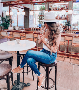 Instagram Fashion by popular US fashion blog, The Sweetest Thing: image of a woman sitting at a bar and wearing a pair of Nordstrom Good Waist Distressed High Waist Ankle Skinny Jeans GOOD AMERICAN, Nordstrom Bridgette Tank FREE PEOPLE, Steve Madden FLORETTA COGNAC LEATHER, and Red Dress The Speckled Grey Mack Hat LACK OF COLOR.