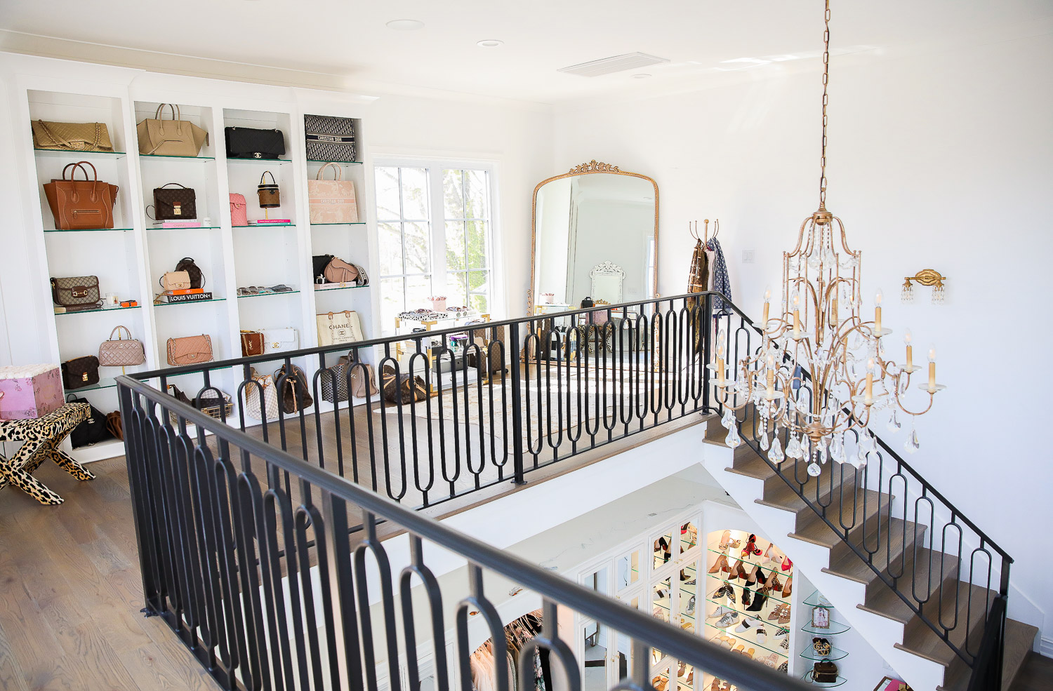 two story closet, emily gemma closet, pinterest designer handbag closet |  Work From Home Outfits by popular US fashion blog, The Sweetest Thing: image of a two story closet with a designer bag display case, gold chandelier, leopard print bench, black metal stair railing, ornate gold full length mirror, and designer shoe display case. 