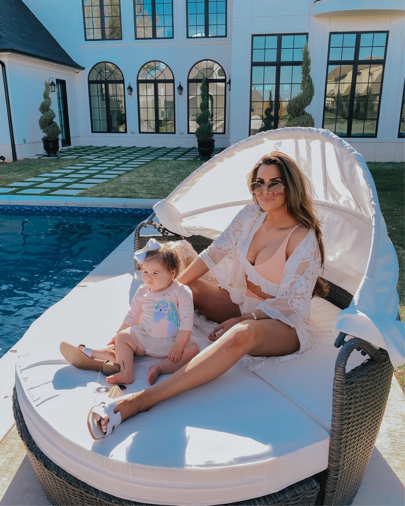 Instagram Recap by popular US life and style blog, The Sweetest Thing: image of Emily Gemma and her daughter Sophie sitting on a shaded pool chair and wearing a unicorn swimsuit, dior sunglasses, Express white lace coverup, Steve Madden white slide sandals, Nadri earrings, The Styled Collection Love necklace, and a peach and white ruffle bikini. 