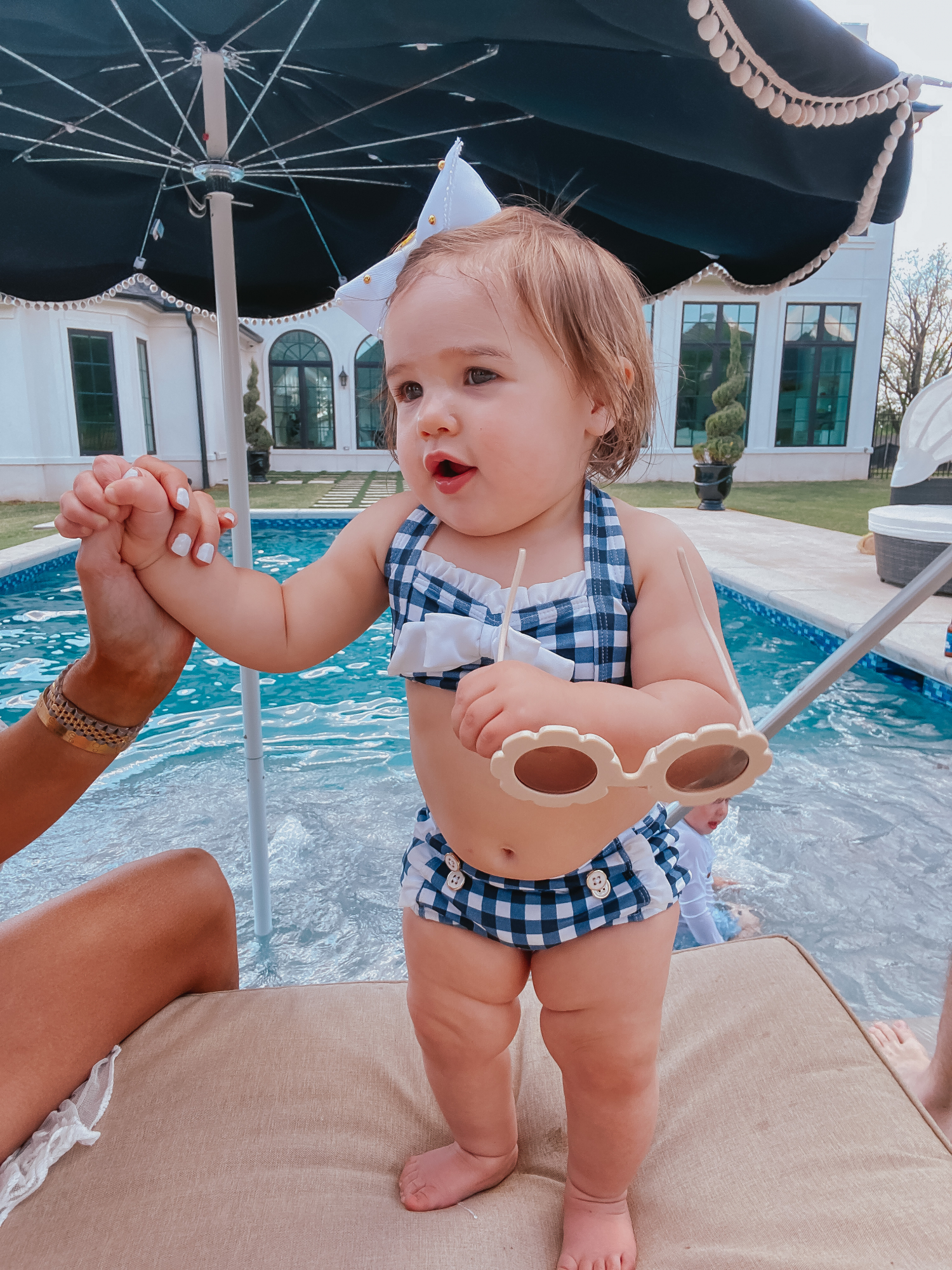Instagram Recap by popular US life and style blog, The Sweetest Thing: image of Emily Gemma's daughter Sophie standing under a One Kings Lane pool umbrella and wearing a Janie and Jack GINGHAM RUFFLE TRIM 2-PIECE SWIMSUIT, Valentina Diaz bow, and holding a pair of Shop Baby Adore Flower Sunglasses.