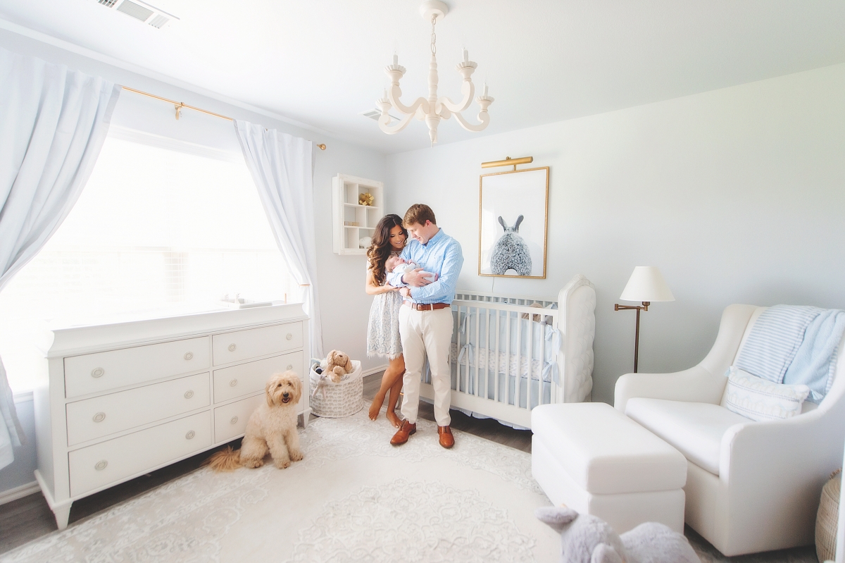 Instagram Recap by popular US life and style blog, The Sweetest Thing: image of Emily Gemma and her husband holding their newborn baby in a nursery with white furniture, white chandelier, black and white bunny print in a gold frame, and a blue and white stripe blanket, 