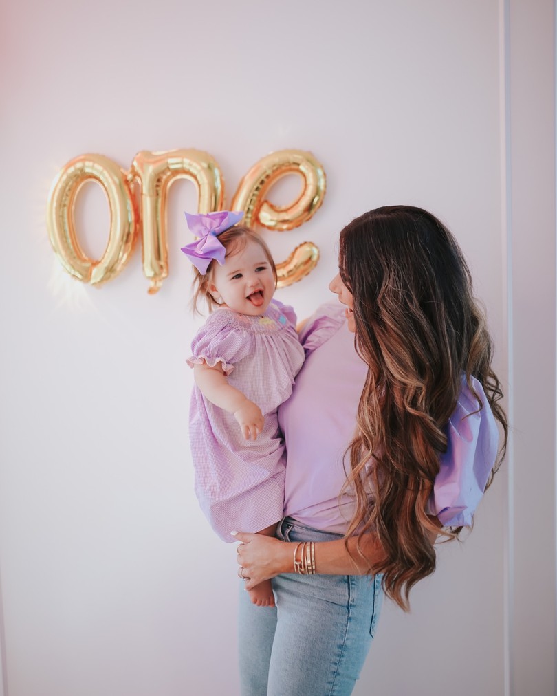 Instagram Recap by popular US life and style blog, The Sweetest Thing: image of Emily Gemma holding her daughter Sophie on her hip in front of a gold 'One' sign and wearing Mother denim, H&M Puff-sleeved Top, and Smocked Auctions SWEET CUPCAKES SMOCKED BISHOP LAVENDER GINGHAM.