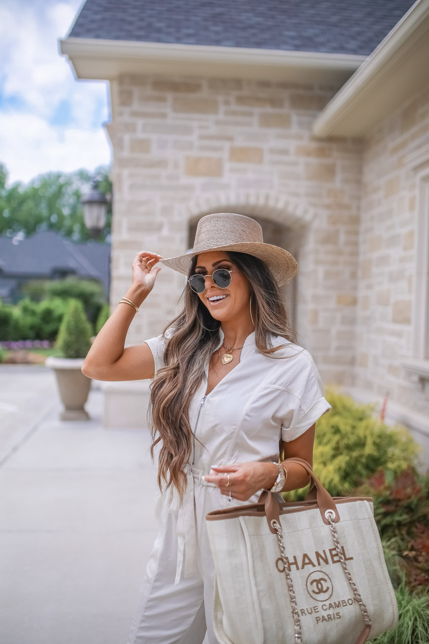 Off White Jumpsuit by popular US fashion blog, The Sweetest Thing: image of a woman wearing a Express Zip Front Utility Jumpsuit, Nordstrom heeled sandals, Express Large Metal Hoop Earrings, Cartier jewelry, a straw hat, and holding a Chanel bag. 