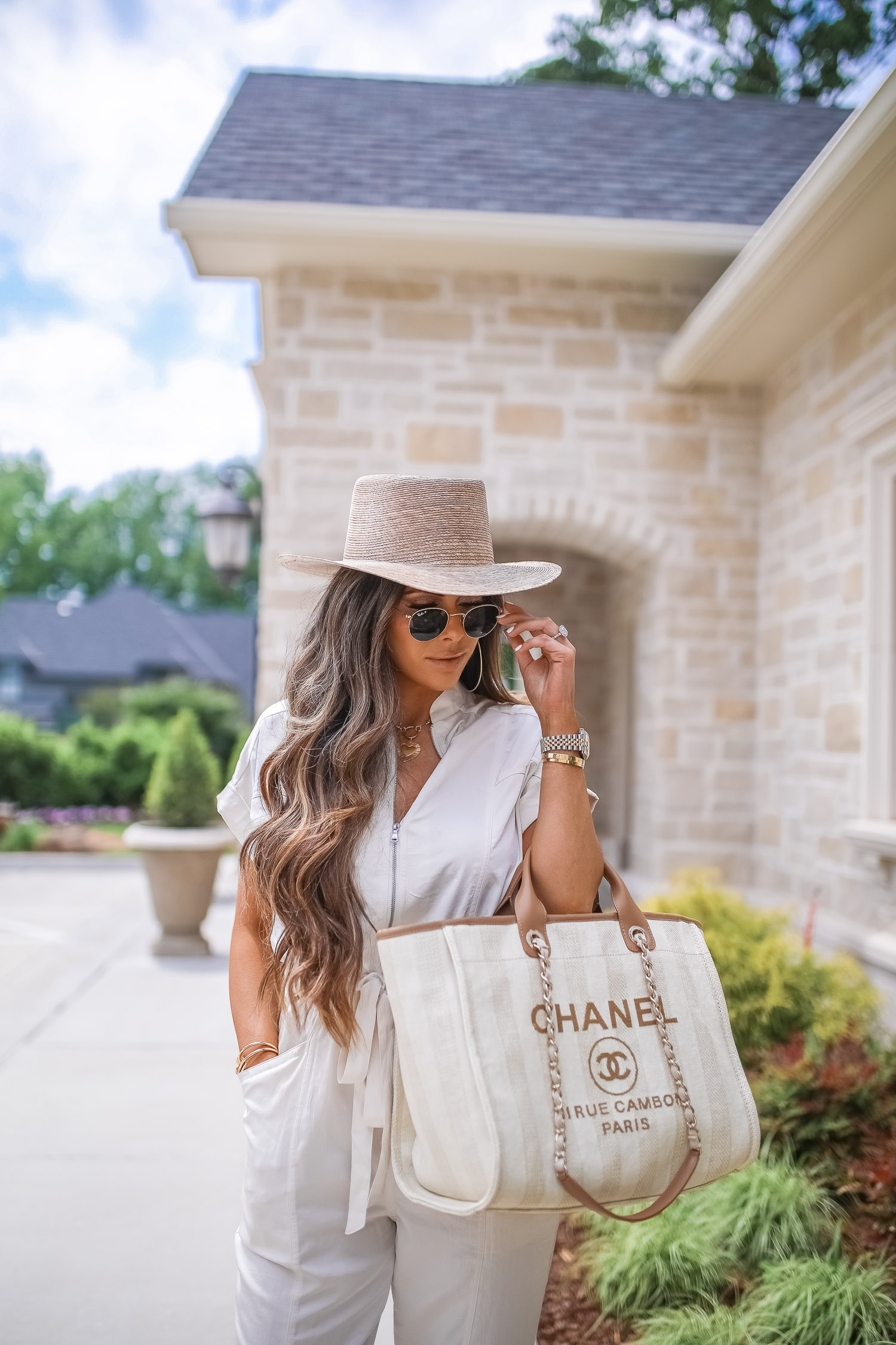 Off White Jumpsuit by popular US fashion blog, The Sweetest Thing: image of a woman wearing a Express Zip Front Utility Jumpsuit, Nordstrom heeled sandals, Express Large Metal Hoop Earrings, Cartier jewelry, a straw hat, and holding a Chanel bag. 