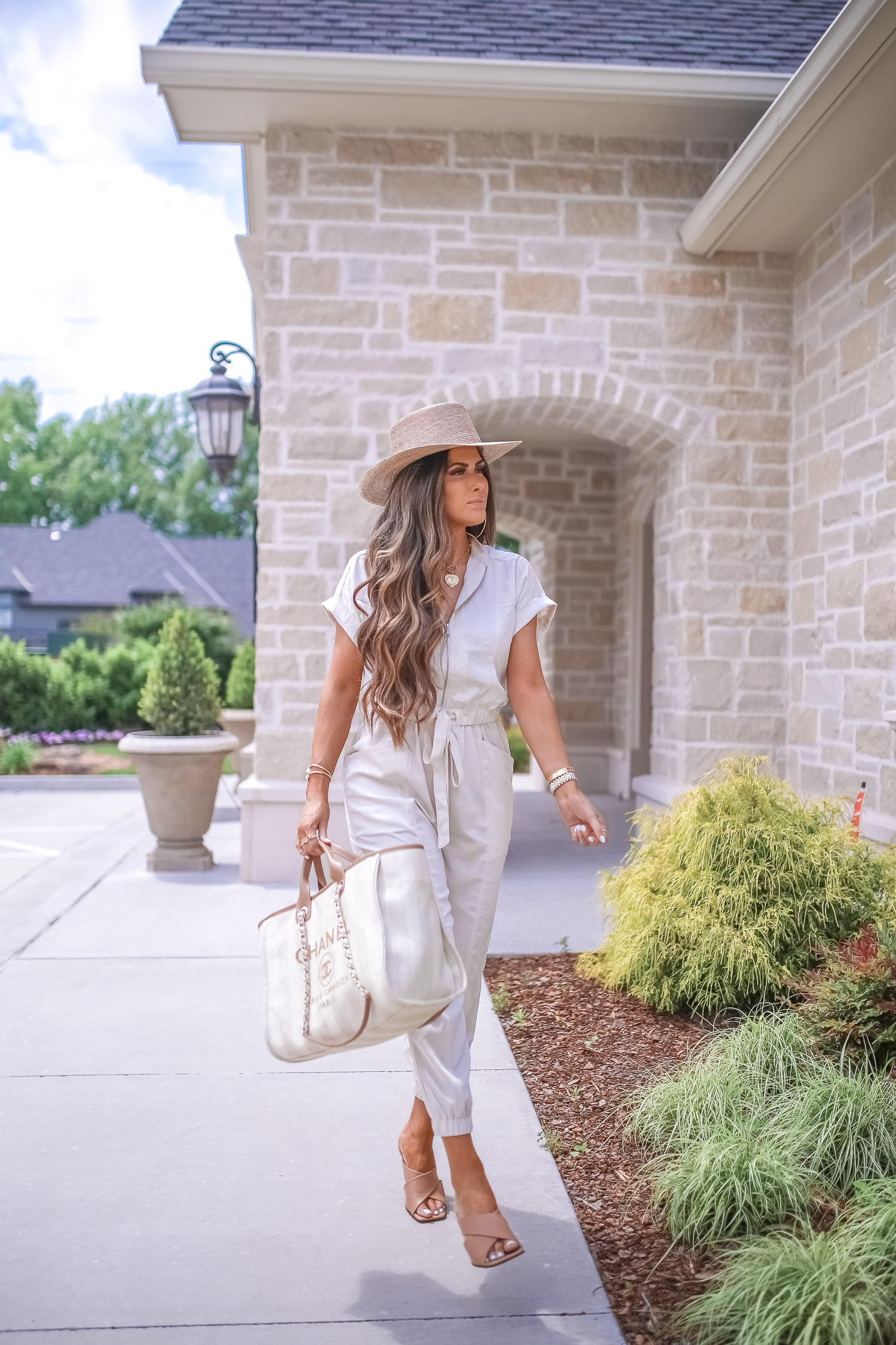 Off White Jumpsuit by popular US fashion blog, The Sweetest Thing: image of a woman wearing a Express Zip Front Utility Jumpsuit, Nordstrom heeled sandals, Express Large Metal Hoop Earrings, Cartier jewelry, a straw hat, and holding a Chanel bag. 