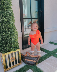 Louis Vuitton Bumbag, Mackenzie Childs, baby swimsuits, cute babies, baby summer style, Emily Gemma | Instagram Recap by popular US life and style blog, The Sweetest Thing: image of Emily Gemma's daughter wearing a red one shoulder ruffle swimsuit and standing next to a Louis Vuitton Monogram Bumbag and Mackenzie-Childs Swirl Topiary.