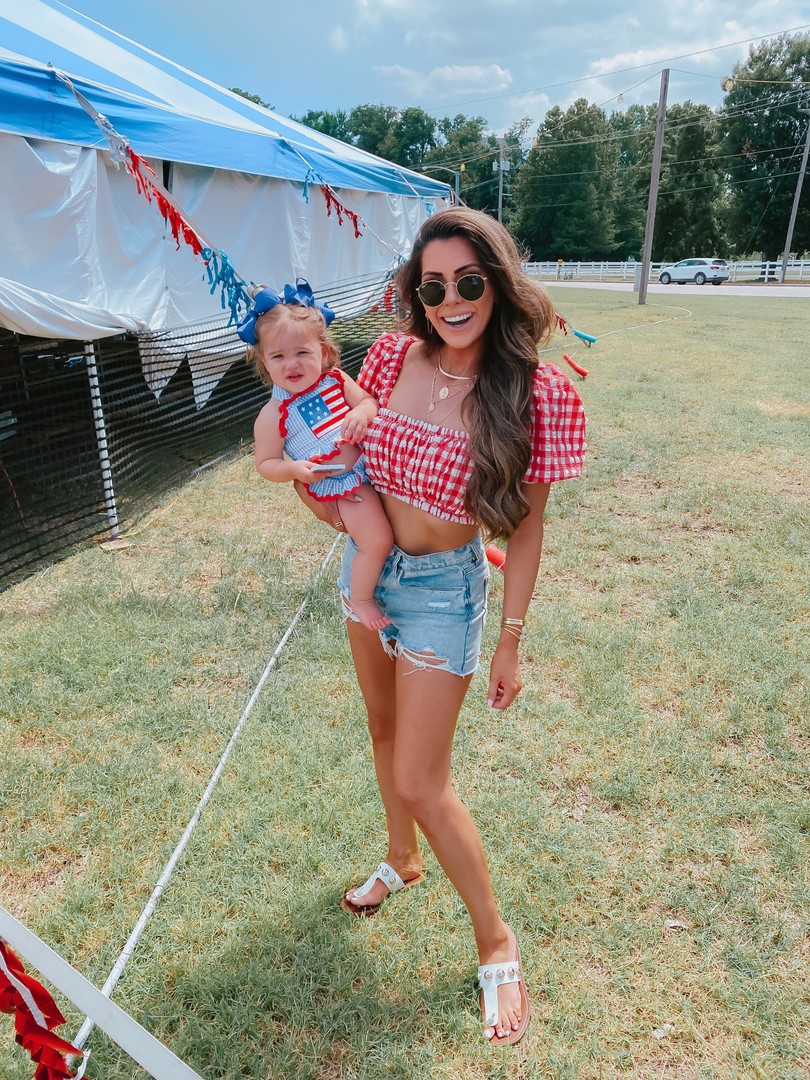 Instagram Recap by popular US life an style blog, The Sweetest Thing: image of Emily Gemma wearing a pair of BLANKNYC shorts, Marc Fisher slide sandals,  Montce red and white gingham crop top, 8 Other Reasons necklace, and Rayban sunglasses while holding her baby daughter that's wearing a smocked auctions swimsuit. 