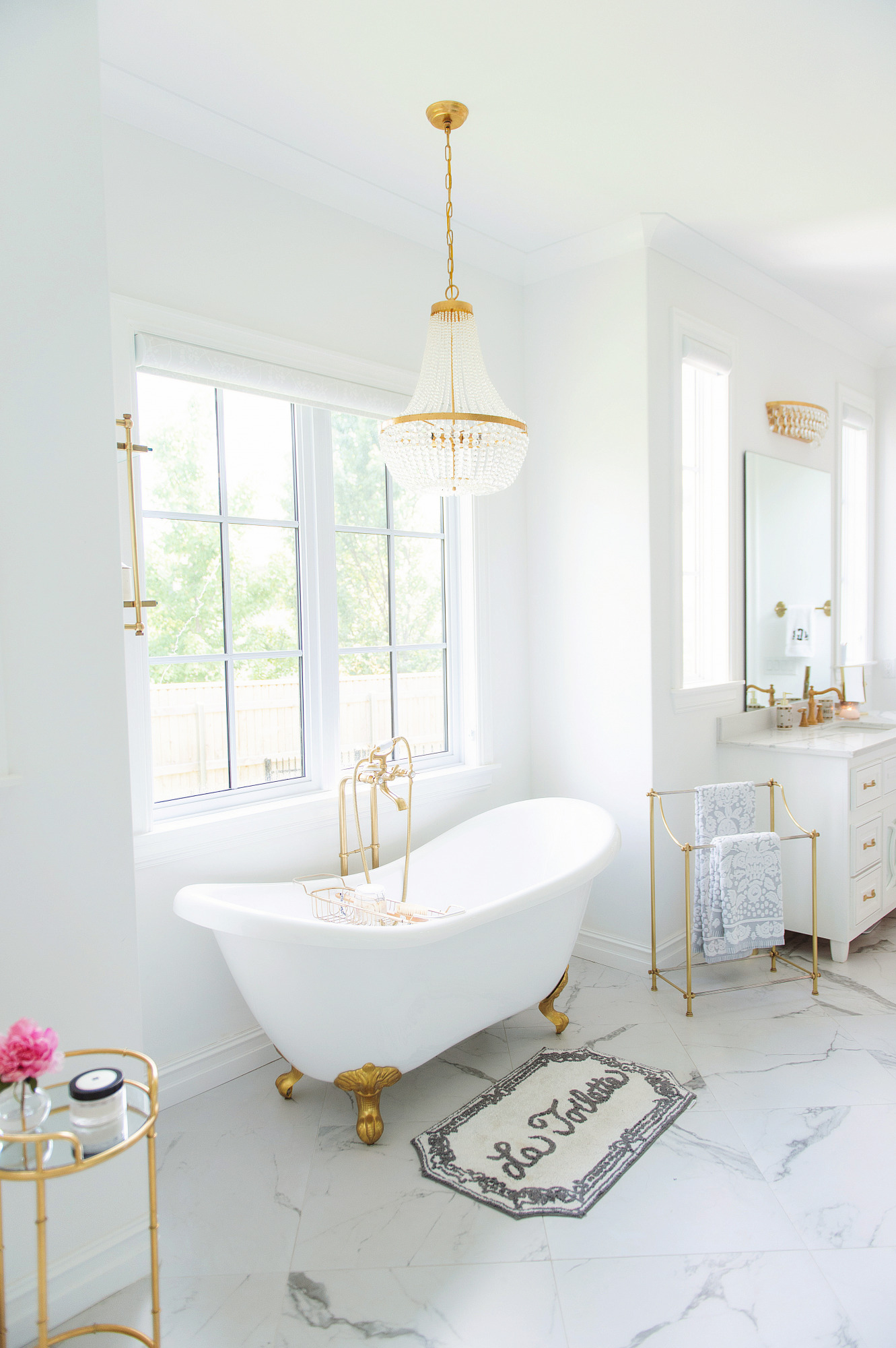 Blog Design by popular US lifestyle blog, The Sweetest Thing: image of a bathroom with a white and gold claw foot tub, chandelier, and white vanity. 
