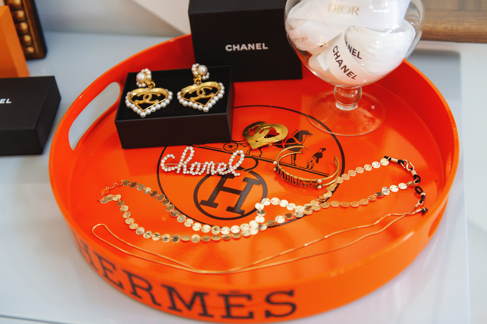 Blog Design by popular US lifestyle blog, The Sweetest Thing: image of a Hermes tray containing Chanel earrings, a Chanel hair clip, and some gold necklaces. 