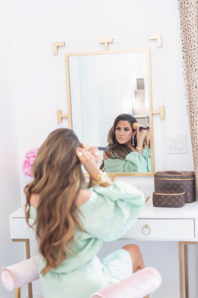 Blog Design by popular US lifestyle blog, The Sweetest Thing: image of Emily Gemma wearing a mint green dress and sitting on a pink velvet bench while she sits at her vanity and applies her makeup. 