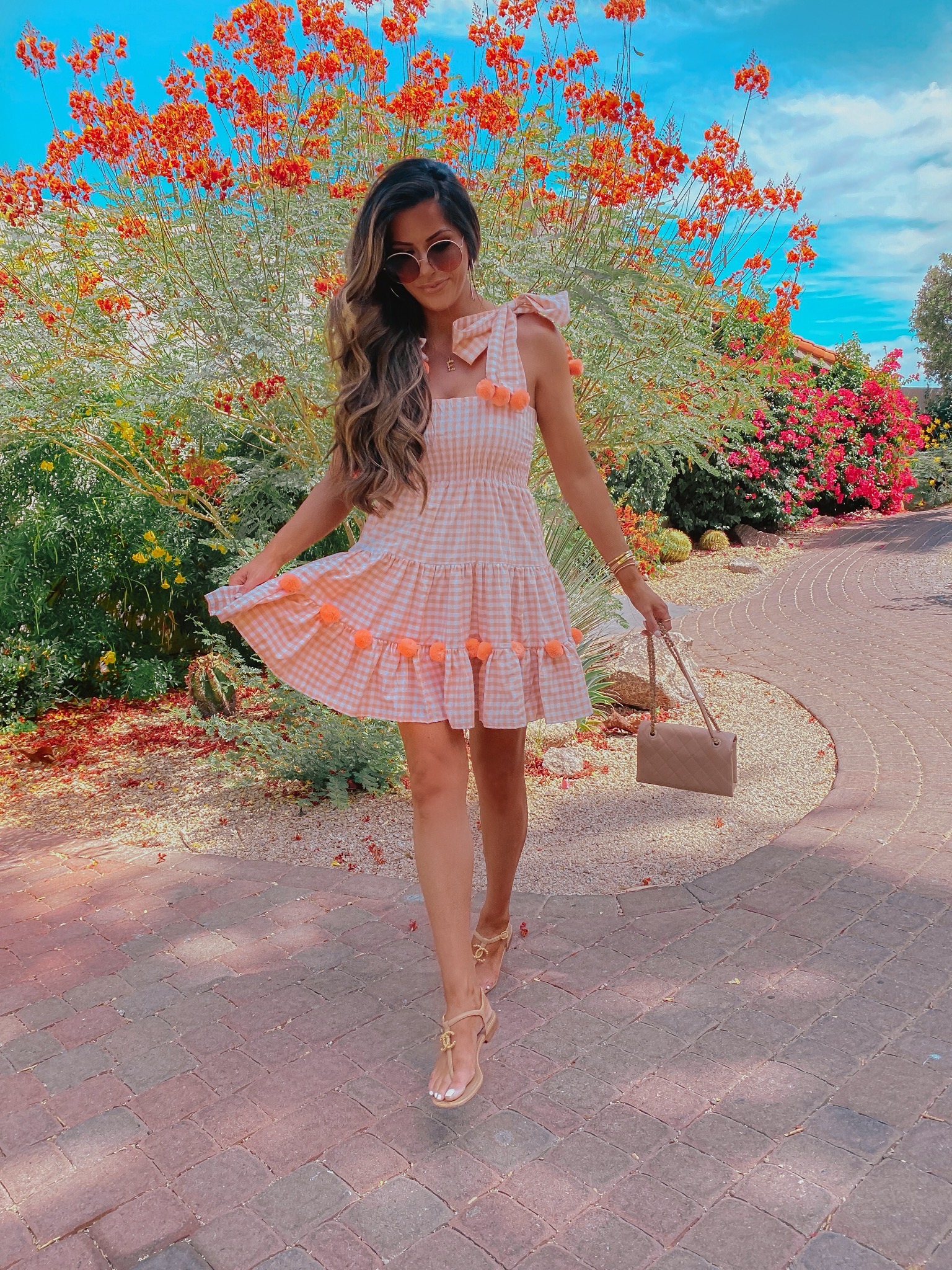 Instagram Recap by popular US life an style blog, The Sweetest Thing: image of Emily Gemma walking outside by a flowering bush and wearing a Pippa orange gingham and pom pom dress, Chanel sandals, Chloe neckalce, Nadri gold hoop earrings, and carrying a Chanel purse. 