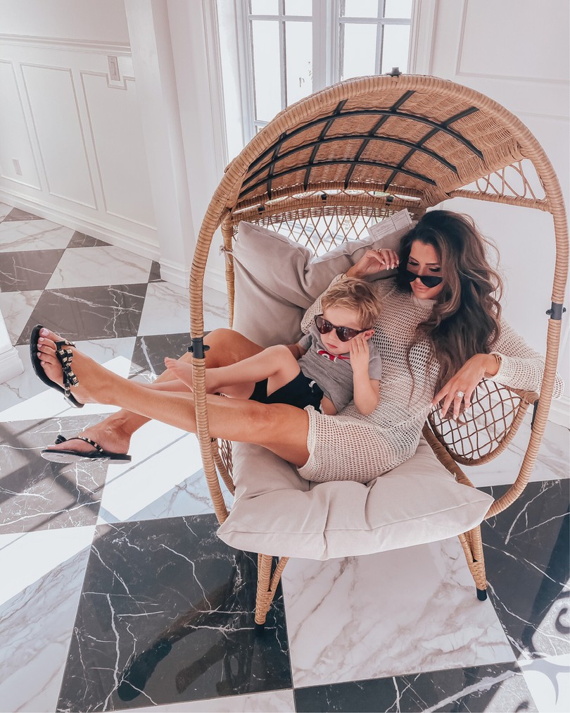  Instagram Recap by popular US life an style blog, The Sweetest Thing: image of Emily Gemma sitting outside in a rattan chair with her son and wearing a The Styled Co faith necklace, Nasty Gal Recycled Crochet to Go Mini Cover-Up Dress, The Styled Co love necklace, The Styled Co crystal pave ring, Zimmermann swimsuit, and Melissa sandals. 