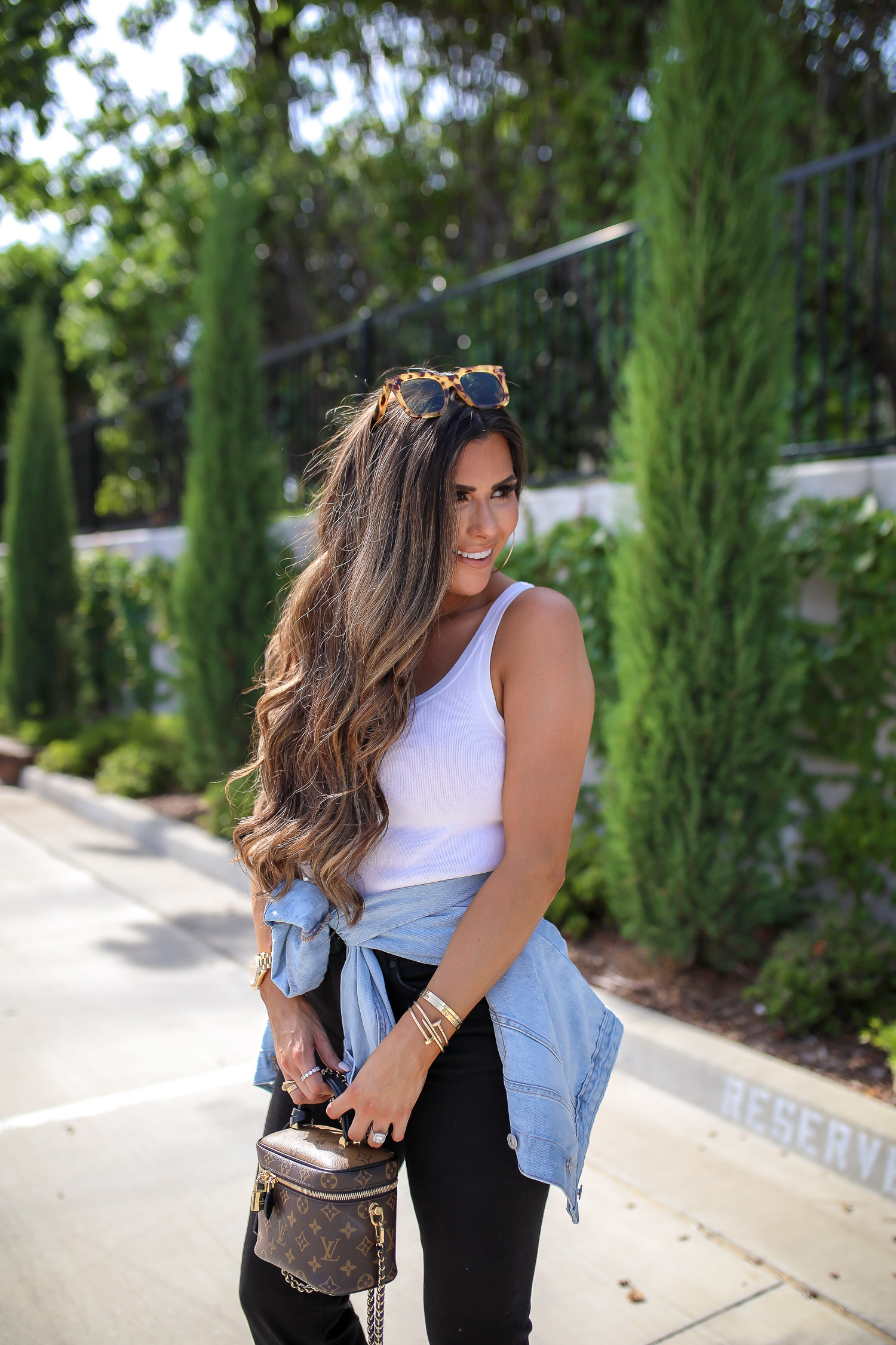 Denim Jacket by popular US fashion blog, The Sweetest Thing: image of Emily Gemma standing outside in a parking lot and wearing a Express Puff Sleeve Light Wash Denim Jacket, Express Scoop Neck Sweater Cami, Express High Waisted Black Raw Hem Cropped Wide Leg Jeans, Express 2" Metal Hoop Earrings, Express Chain Ankle Bracelet, Cartier bracelets, Bottega Veneta shoes and holding a Louis Vuitton purse. 