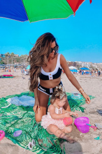 summer fashion 2020, swimsuit outfits, beach outfits, Emily Ann Gemma |Instagram Recap by popular US life and style blog, The Sweetest Thing: image of Emily Gemma sitting on the sand with her daughter while at the beach and wearing a black an white bikini. 