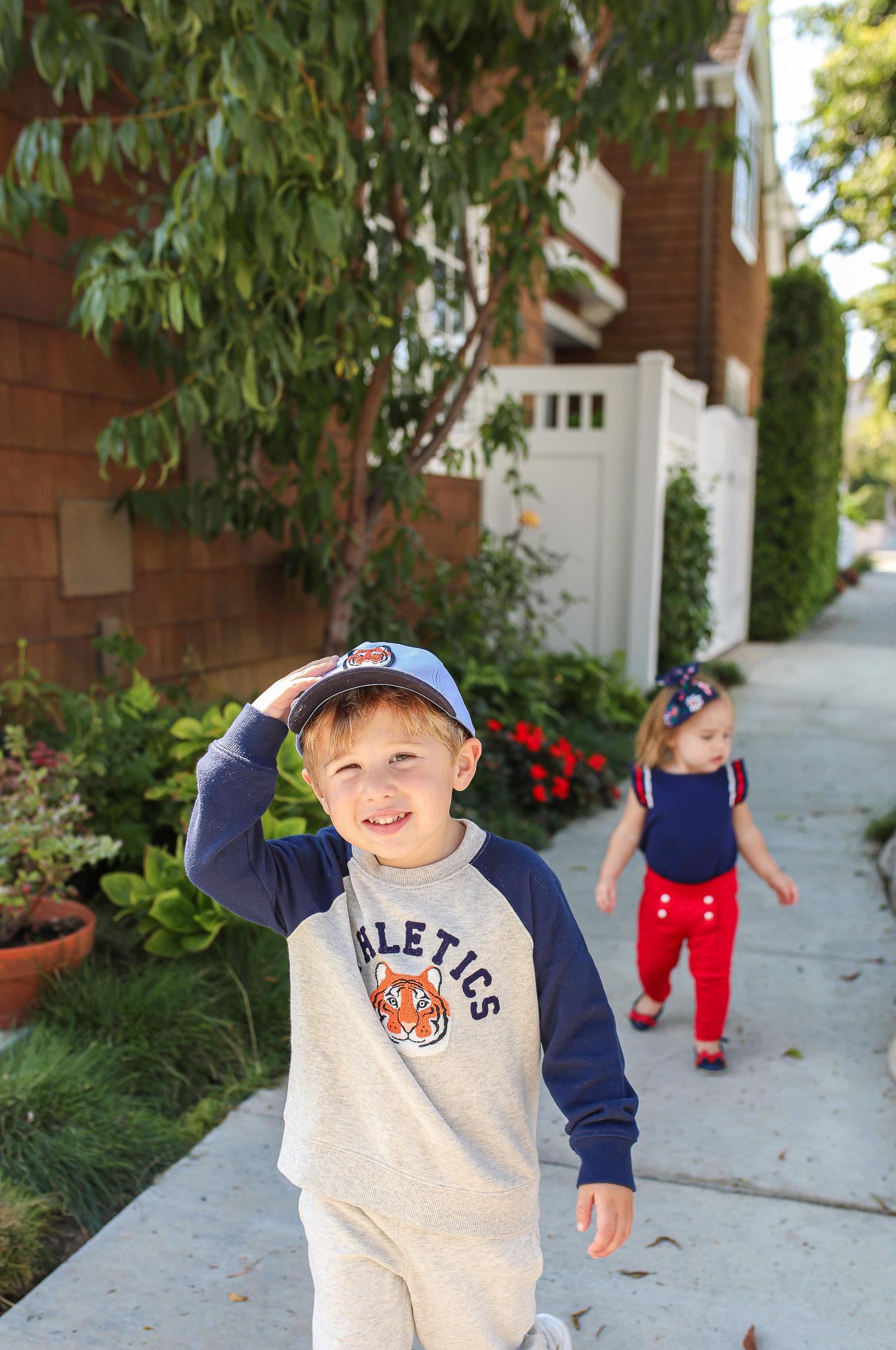 Janie and Jack by popular US fashion Blog, The Sweetest Thing: image of two kids walking outside on a sidewalk in Newport Beach, CA and wearing a Janie and Jack TIGER PATCH CAP, Janie and Jack RAGLAN TIGER SWEATSHIRT, Janie and Jack STRIPE TRIM JOGGER, Janie and Jack PLEATED SLEEVE TOP, Janie and Jack BUTTON PONTE PANT, Janie and Jack BOW ANKLE STRAP FLAT, FLORAL BOW BARRETTE, and Janie and Jack BOUCLÉ PURSE.