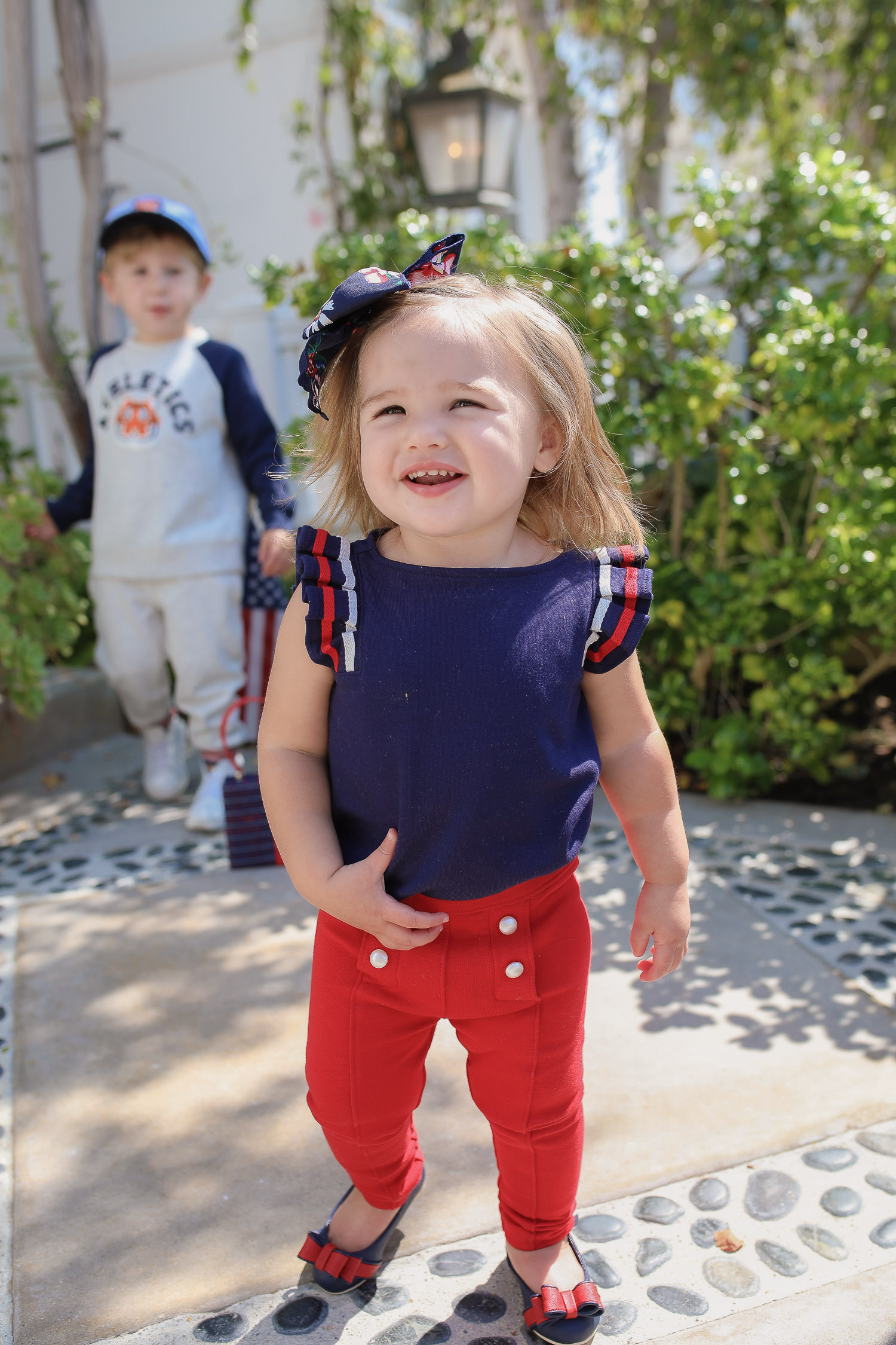 Janie and Jack by popular US fashion Blog, The Sweetest Thing: image of two kids walking outside on a sidewalk in Newport Beach, CA and wearing a Janie and Jack TIGER PATCH CAP, Janie and Jack RAGLAN TIGER SWEATSHIRT, Janie and Jack STRIPE TRIM JOGGER, Janie and Jack PLEATED SLEEVE TOP, Janie and Jack BUTTON PONTE PANT, Janie and Jack BOW ANKLE STRAP FLAT, FLORAL BOW BARRETTE, and Janie and Jack BOUCLÉ PURSE.