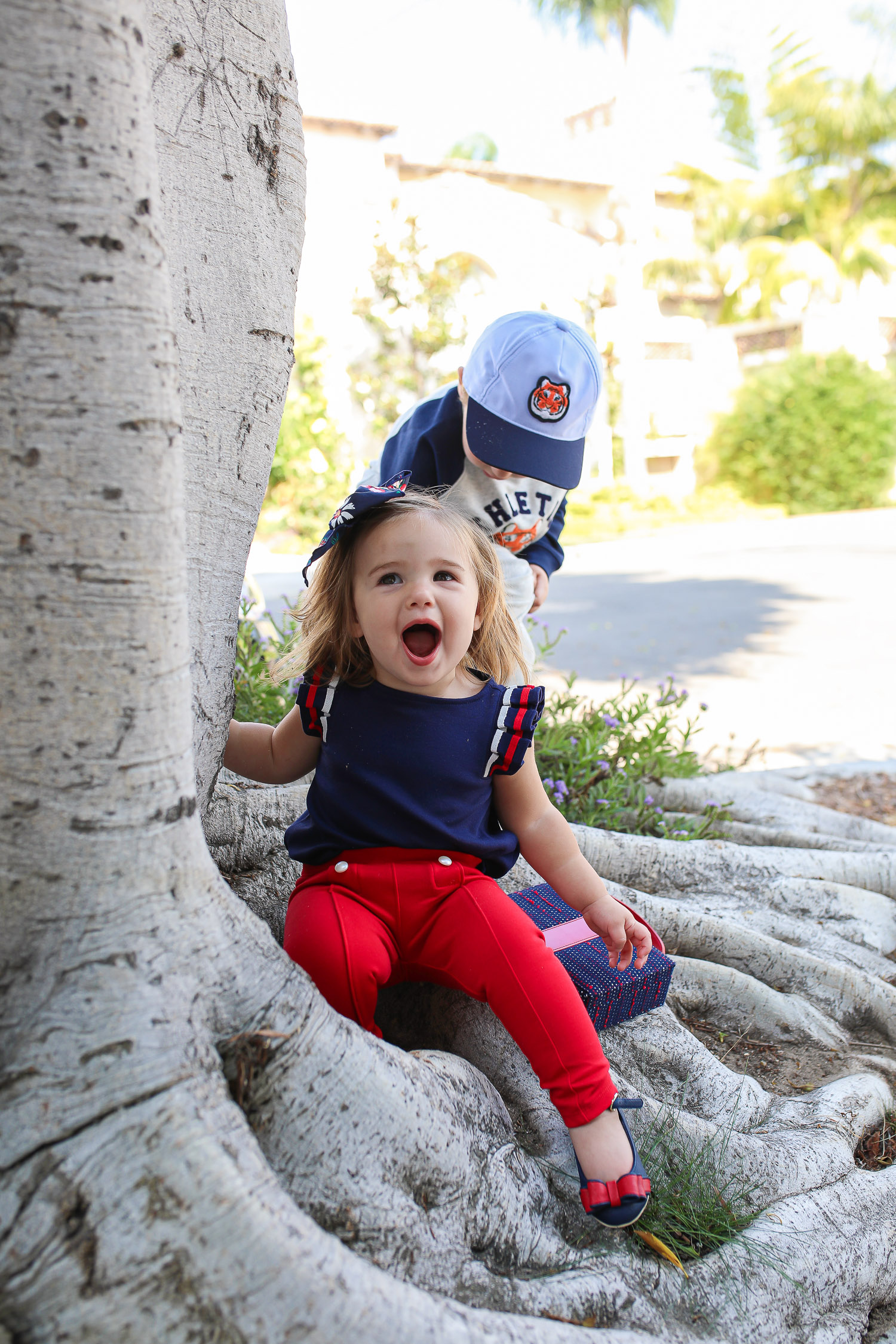 Janie and Jack by popular US fashion Blog, The Sweetest Thing: image of two kids walking outside on a sidewalk in Newport Beach, CA and wearing a Janie and Jack TIGER PATCH CAP, Janie and Jack RAGLAN TIGER SWEATSHIRT, Janie and Jack STRIPE TRIM JOGGER, Janie and Jack PLEATED SLEEVE TOP, Janie and Jack BUTTON PONTE PANT, Janie and Jack BOW ANKLE STRAP FLAT, FLORAL BOW BARRETTE, and Janie and Jack BOUCLÉ PURSE.