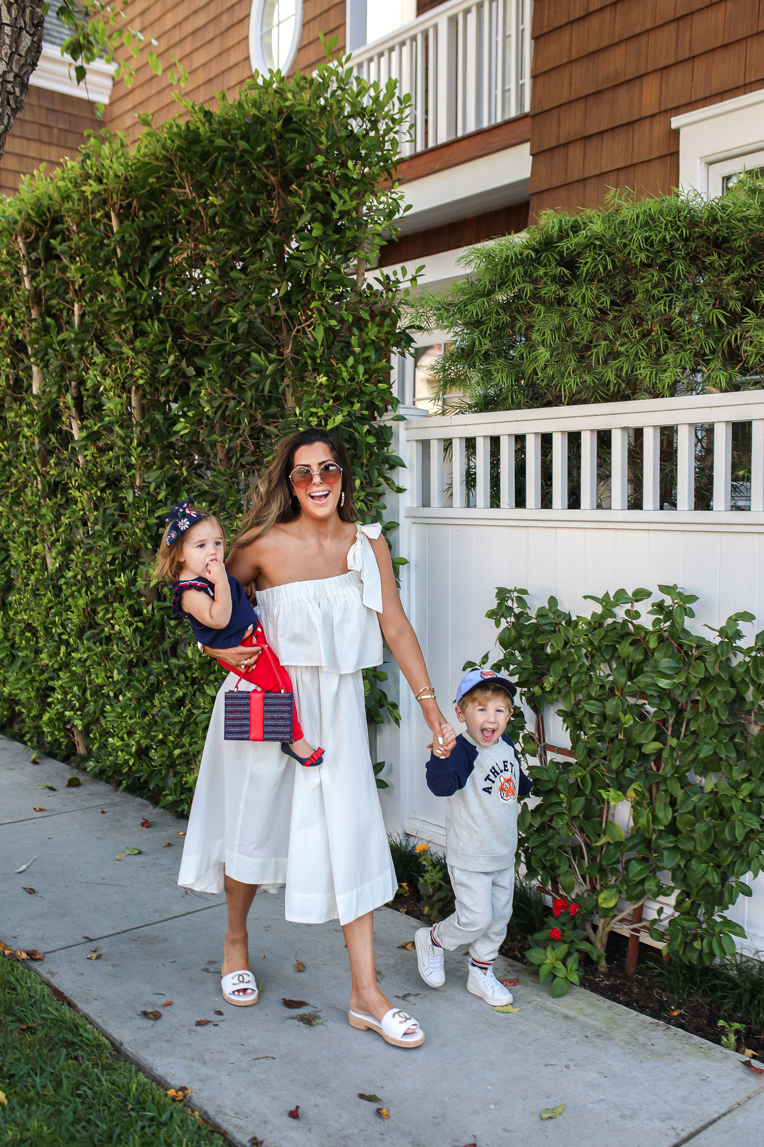 Janie and Jack by popular US fashion Blog, The Sweetest Thing: image of a mom and her two kids walking outside on a sidewalk in Newport Beach, CA and wearing a white one shoulder dress and white Channel slide sandals, Janie and Jack TIGER PATCH CAP, Janie and Jack RAGLAN TIGER SWEATSHIRT, Janie and Jack STRIPE TRIM JOGGER, Janie and Jack PLEATED SLEEVE TOP, Janie and Jack BUTTON PONTE PANT, Janie and Jack BOW ANKLE STRAP FLAT, FLORAL BOW BARRETTE, and Janie and Jack BOUCLÉ PURSE.