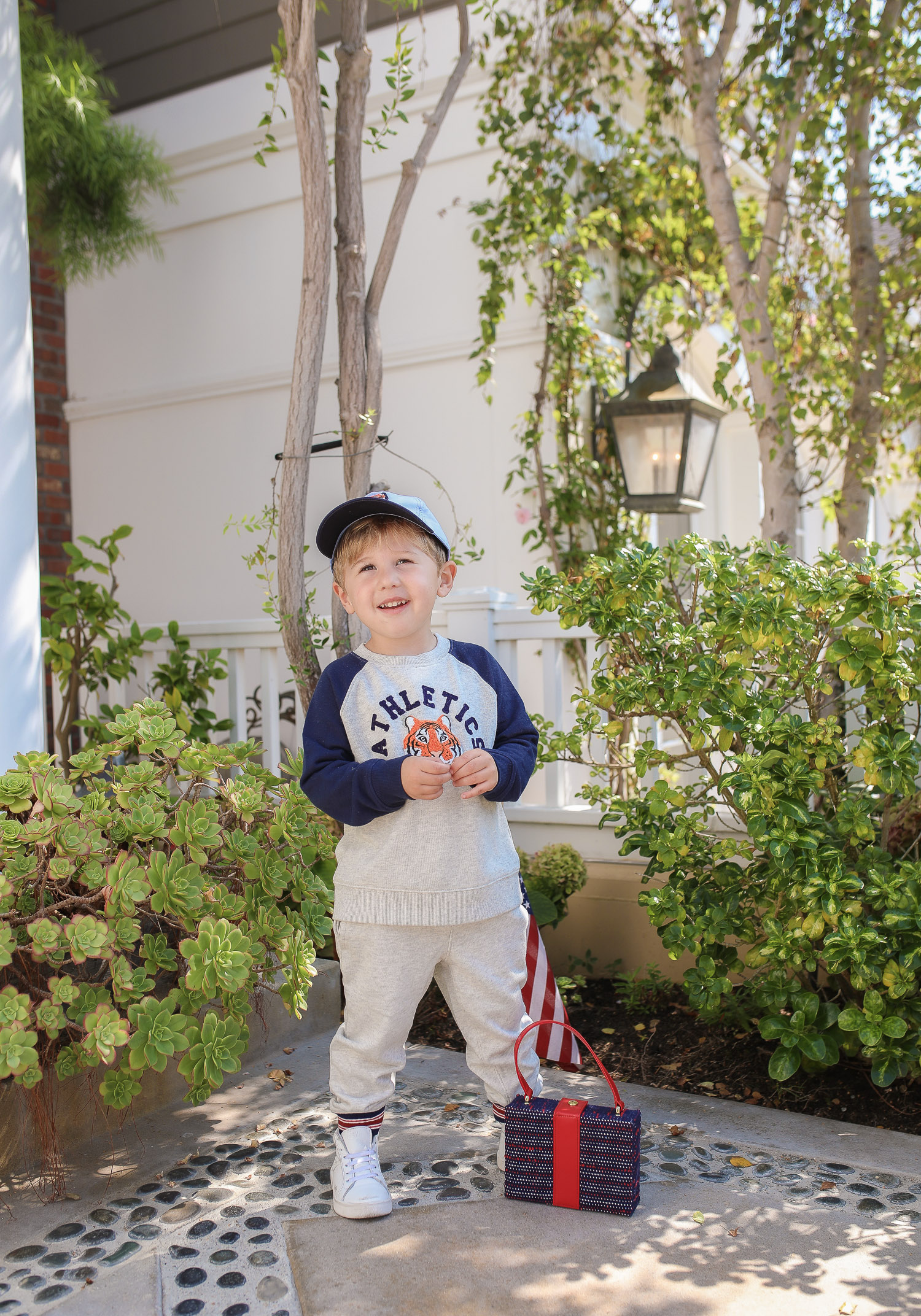 Janie and Jack by popular US fashion Blog, The Sweetest Thing: image of a young boy sitting outside on the ground in Newport Beach, CA and wearing a Janie and Jack TIGER PATCH CAP, Janie and Jack RAGLAN TIGER SWEATSHIRT, Janie and Jack STRIPE TRIM JOGGER.
