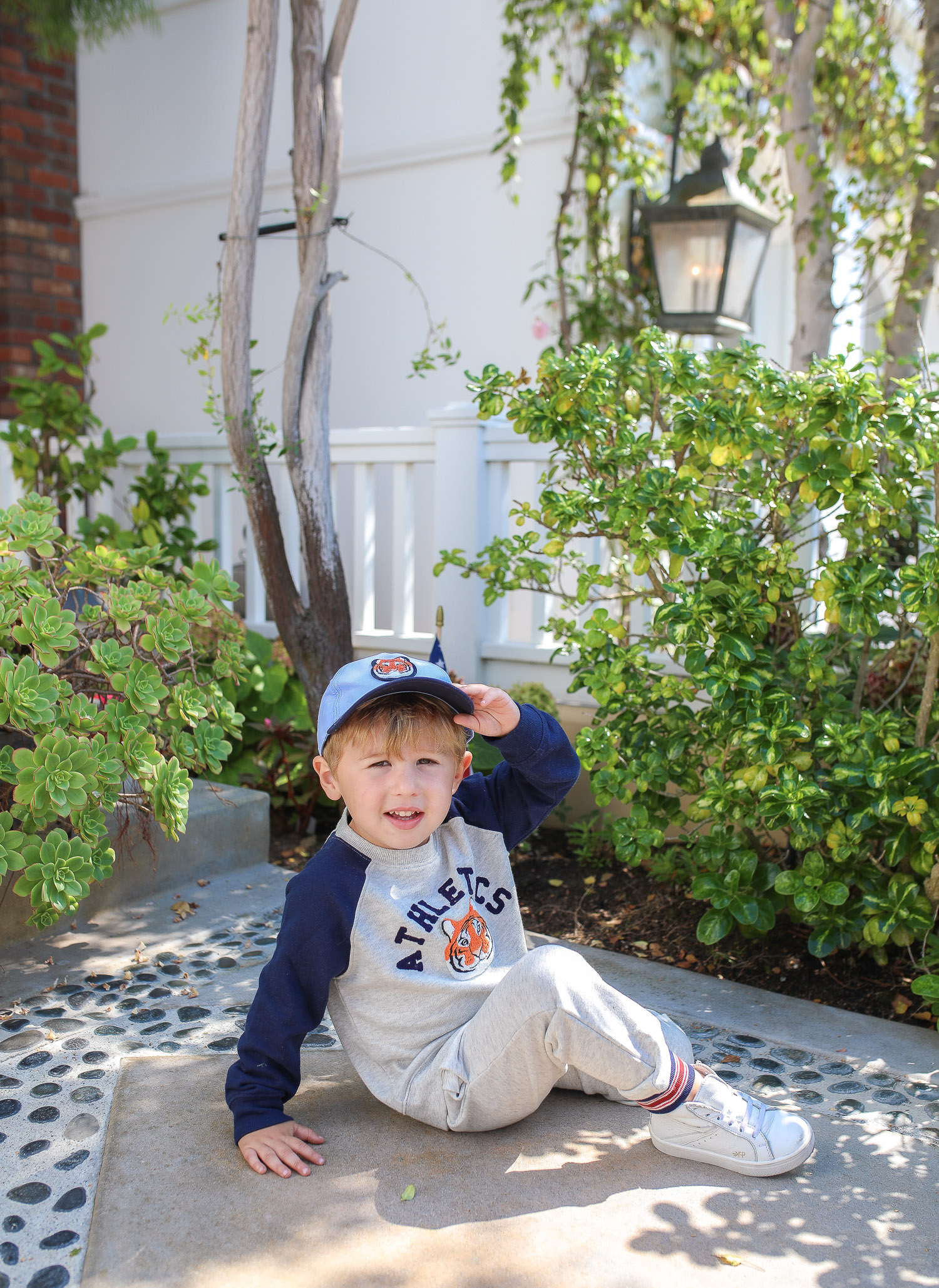 Janie and Jack by popular US fashion Blog, The Sweetest Thing: image of a young boy sitting outside on the ground in Newport Beach, CA and wearing a Janie and Jack TIGER PATCH CAP, Janie and Jack RAGLAN TIGER SWEATSHIRT, Janie and Jack STRIPE TRIM JOGGER.