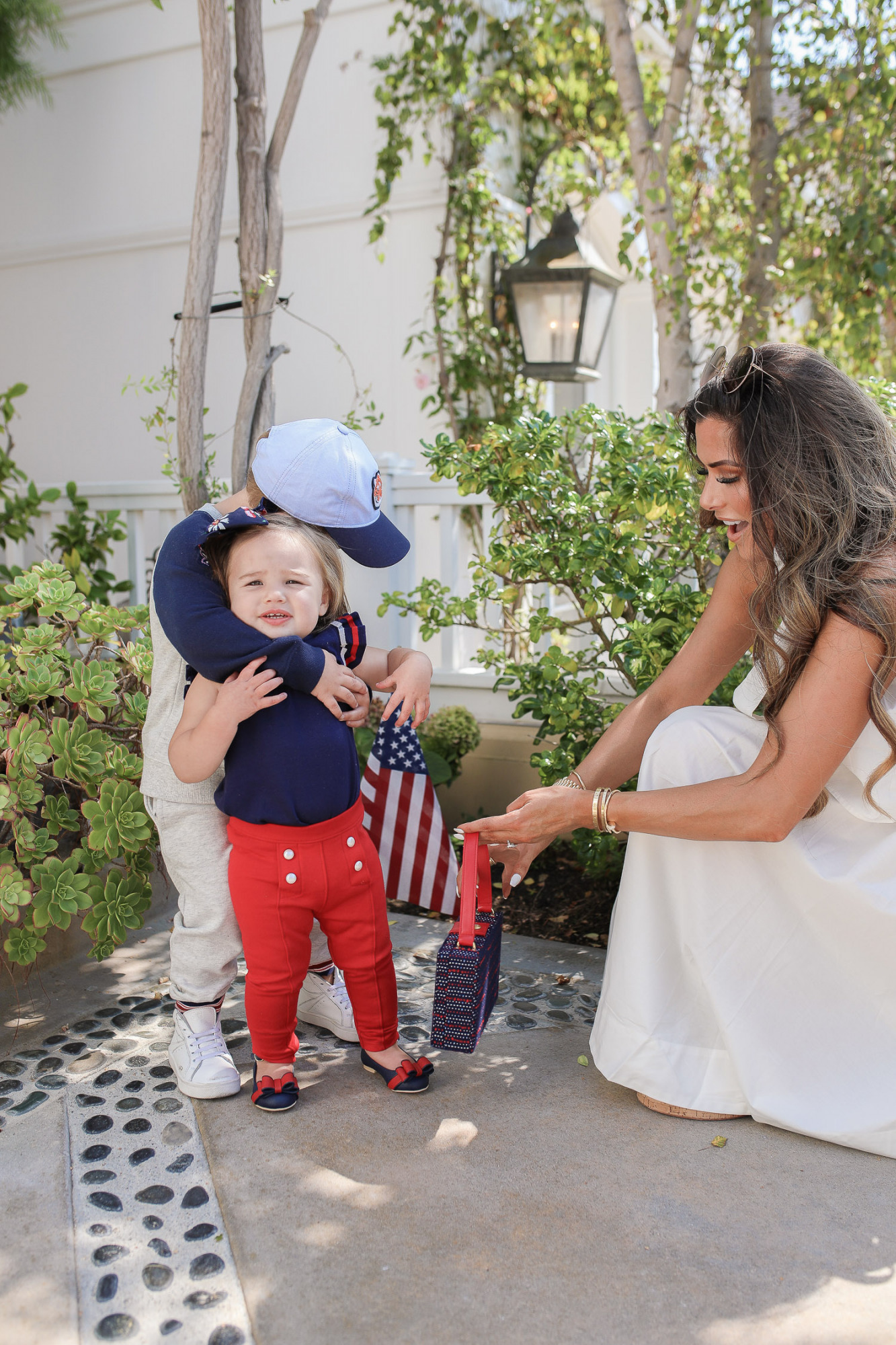 Janie and Jack by popular US fashion Blog, The Sweetest Thing: image of a mom and her two kids walking outside on a sidewalk in Newport Beach, CA and wearing a white one shoulder dress and white Channel slide sandals, Janie and Jack TIGER PATCH CAP, Janie and Jack RAGLAN TIGER SWEATSHIRT, Janie and Jack STRIPE TRIM JOGGER, Janie and Jack PLEATED SLEEVE TOP, Janie and Jack BUTTON PONTE PANT, Janie and Jack BOW ANKLE STRAP FLAT, FLORAL BOW BARRETTE, and Janie and Jack BOUCLÉ PURSE.