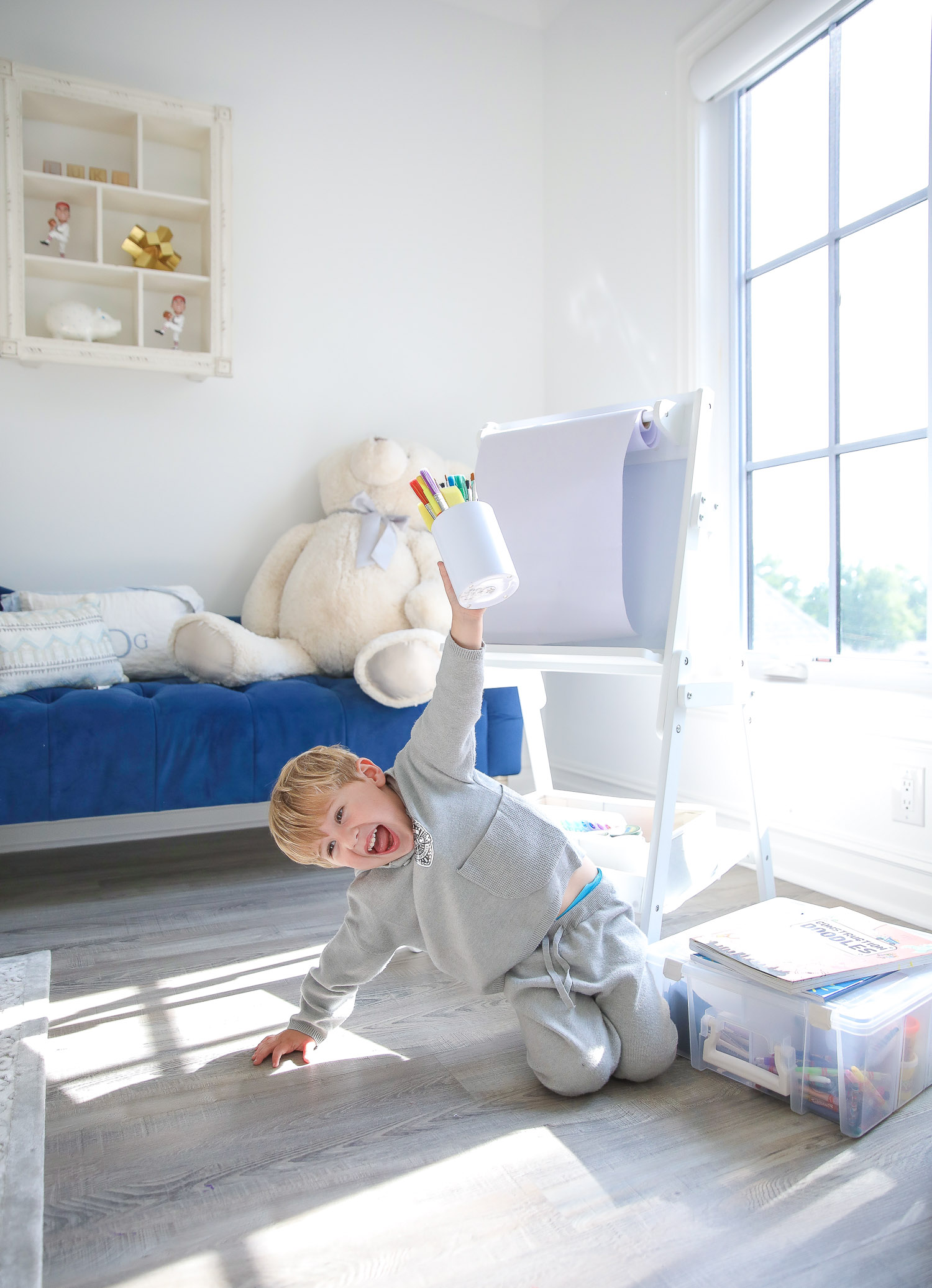 walmart kids home organization must haves, playroom organization ideas, emily gemma, the sweetest thing blog | Playroom Organization by popular US life and style blog, The Sweetest Thing: image of a little boy sitting on the floor in front of a Walmart Delta Children Classic Kids Whiteboard/Dry Erase Easel with Paper Roll and Storage, clear storage bins, and holding a white container filled with Walmart Go Create Assorted Paint Brushes