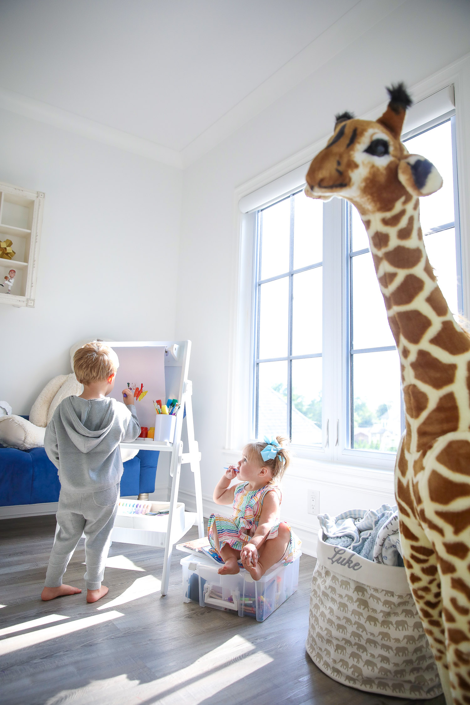 walmart kids home organization must haves, playroom organization ideas, emily gemma, the sweetest thing blog | Playroom Organization by popular US life and style blog, The Sweetest Thing: image of a little boy and girl in a playroom with a Walmart Delta Children Classic Kids Whiteboard/Dry Erase Easel with Paper Roll and Storage, clear storage bins, and holding a white container filled with Walmart Go Create Assorted Paint Brushes