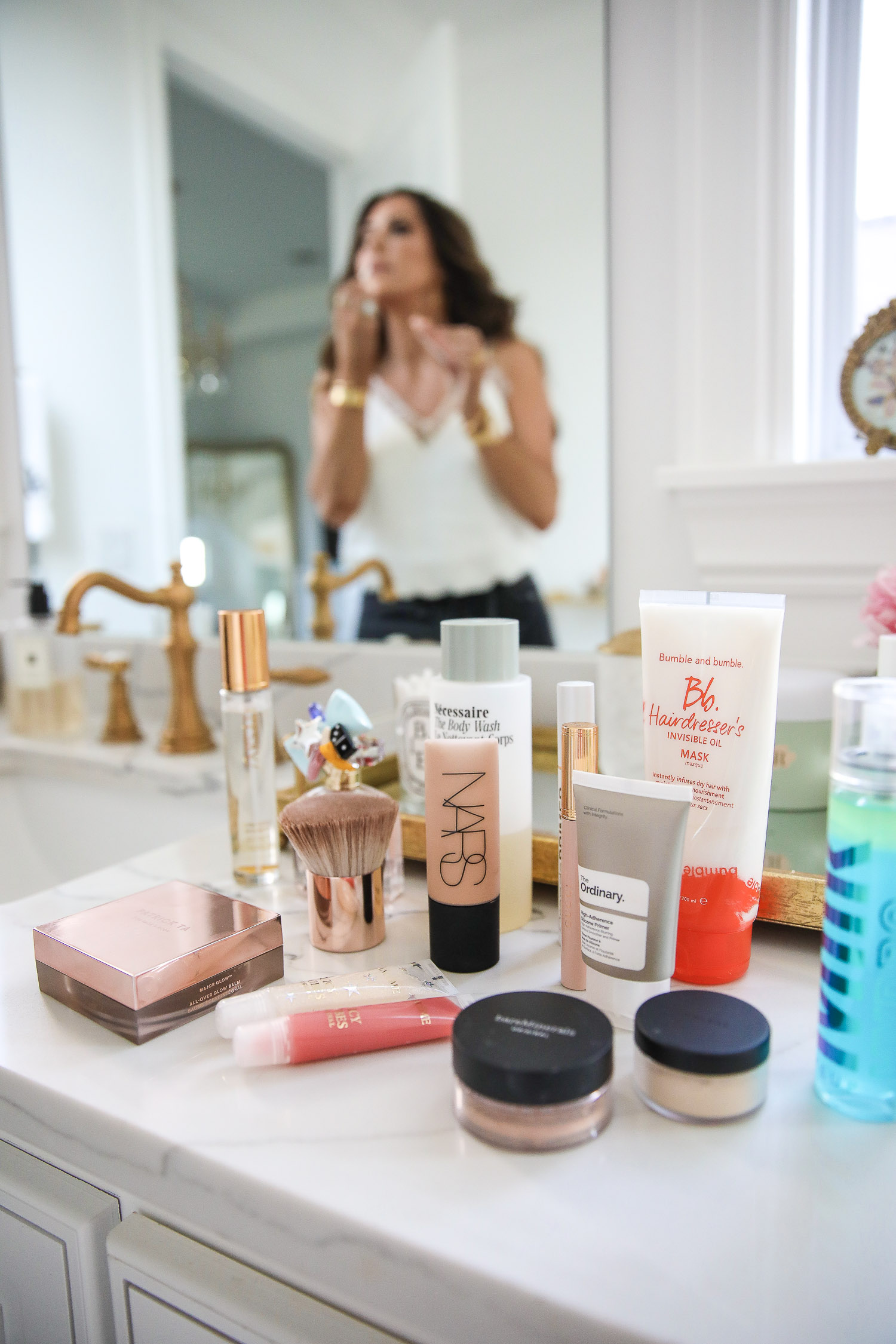 Sephora Favorites by popular US beauty blog, The Sweetest Thing: image of Nars foundation, The Ordinary primer, Bare Minerals powder, Milk makeup setting spray, lip gloss, and powder brush on a marble bathroom vanity counter. 