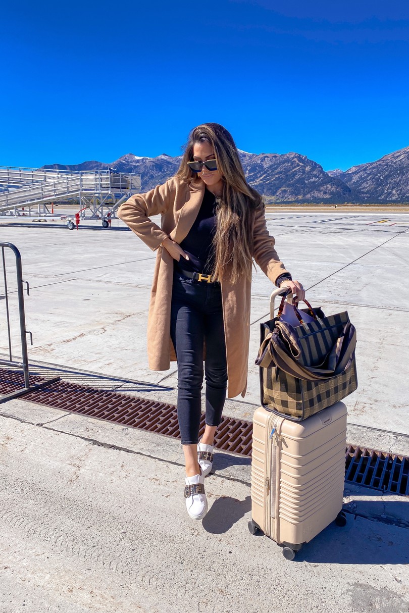 Instagram Recap by popular US lifestyle blog, The Sweetest Thing: image of Emily Gemma standing on a runway strip next to a Beis suitcase, and wearing Louis Vuitton sunglasses, Hermes belt, Bracha necklace, Good American jeans, Express coat and Fendi sneakers. 
