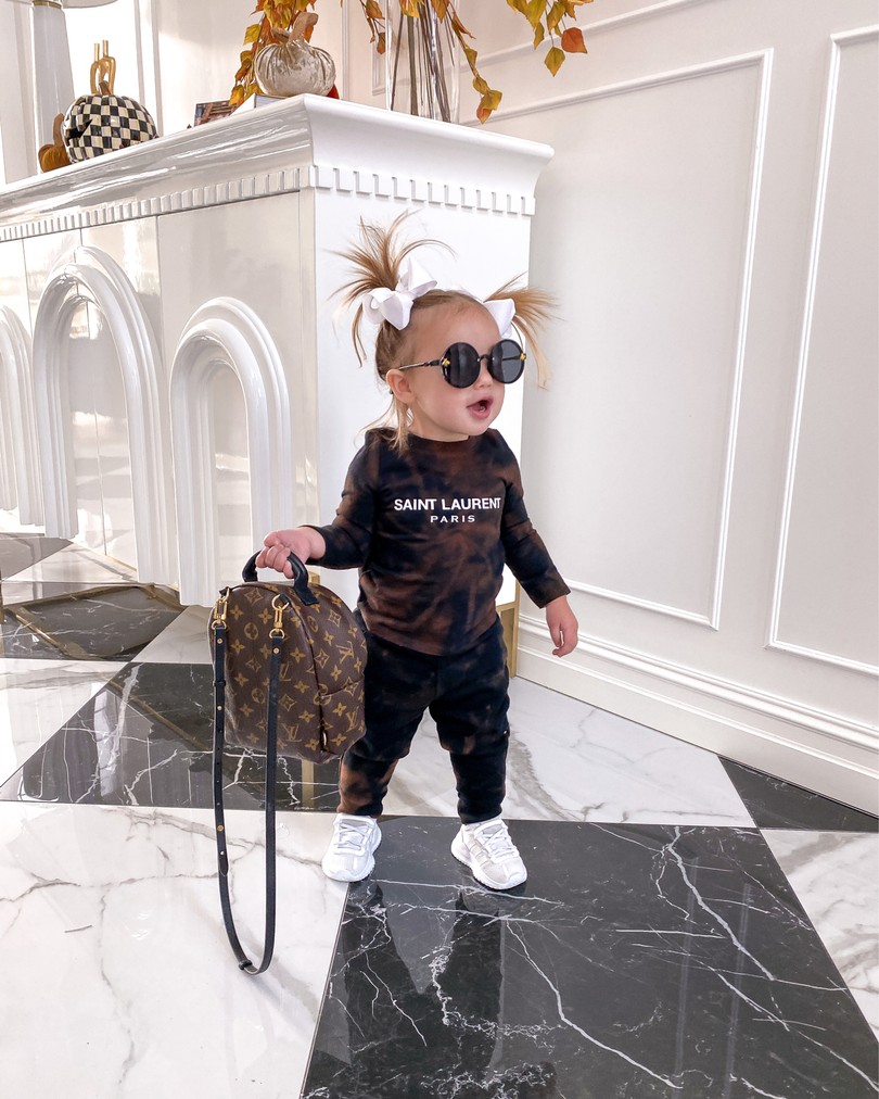 fall home decor, Sophia gemma, toddler fashion, toddler style, tie dye sweatsuit, Louis Vuitton backpack |  Instagram Recap by popular US life and style blog, The Sweetest Thing: image of a little girl wearing a brown and black tie dye Saint Laurent loungewear set, white sneakers, white hair bows, round frame sunglasses, and holding a Louis Vuitton backpack. 