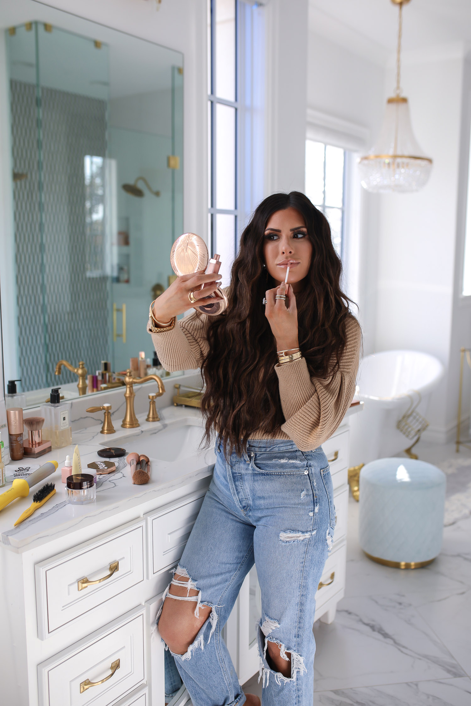 Sephora savings event fall 2020, beauty blogger sephora favorites fall 2020, emily ann gemma |Sephora Beauty Insider Sale by popular US beauty blog, The Sweetest Thing: image of Emily Gemma wearing a puff sleeve turtleneck sweater, Rolex watch, high waist distressed jeans and standing next to her bathroom vanity while looking in a compact mirror and applying some lipgloss.