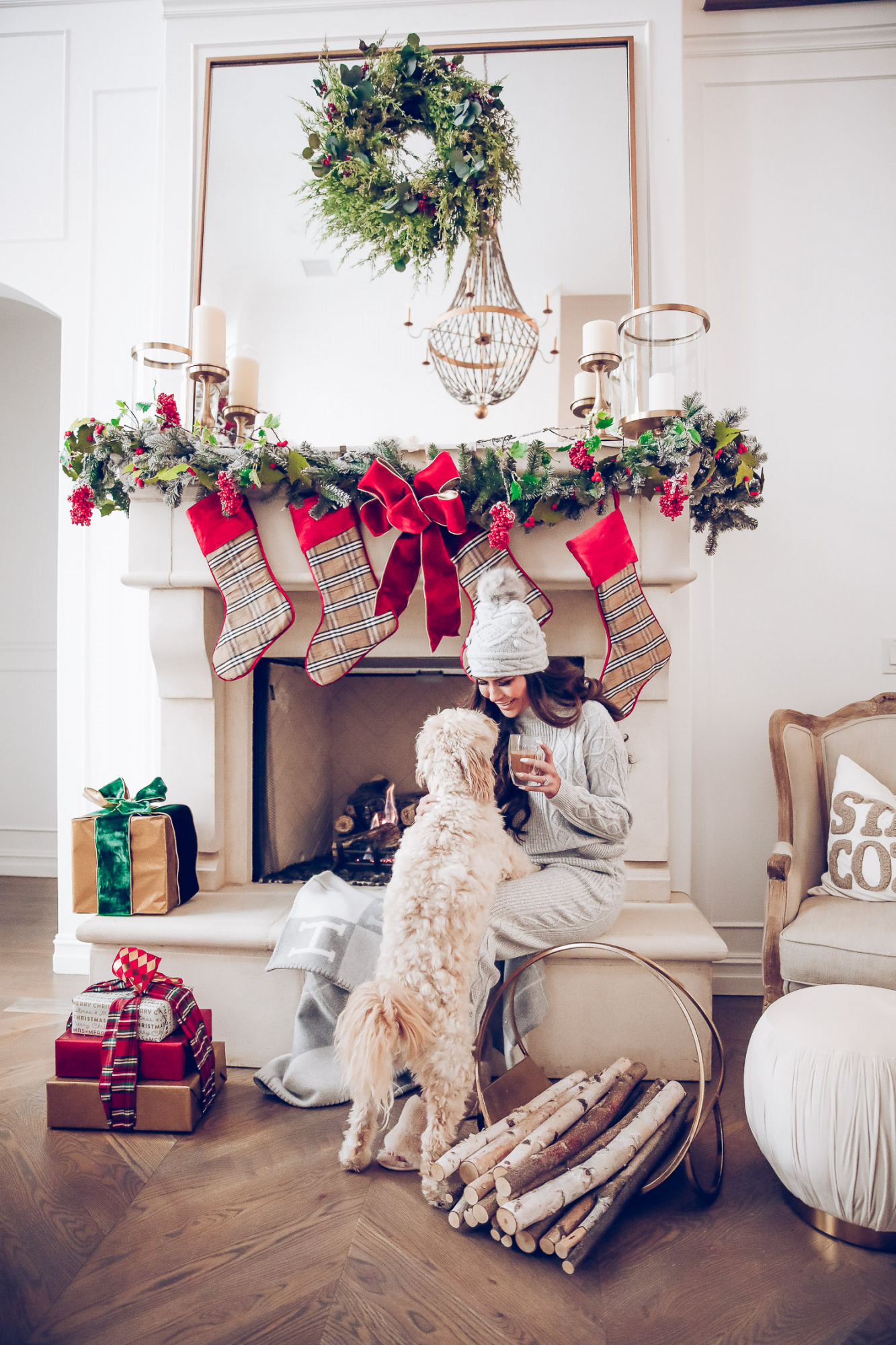 Express loungewear holiday 2020, express sweatsuit december 2020, emily gemma, holiday fireplace garland christmas |Cute Loungewear by popular US fashion blog, The Sweetest Thing: image of Emily Gemma sitting in front of a fireplace decorated with a garland, plaid stockings, and wrapped presents and wearing an Express sweater, Express pants, Express fuzzy slippers, and an Express pom beanie.