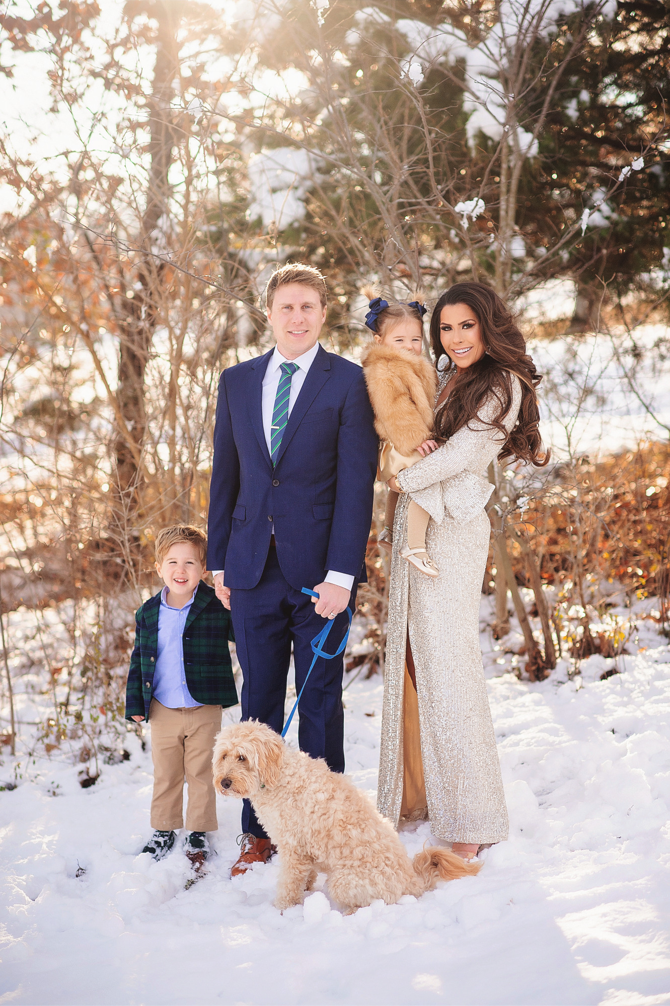 Family Christmas Card by popular US lifestyle blog, The Sweetest Thing: image of a family standing together in the snow with their dog and wearing a Eliza J sequin dress, blue suit, blue and green plaid blazer and tan pants, and a faux fur coat and gold dress. 