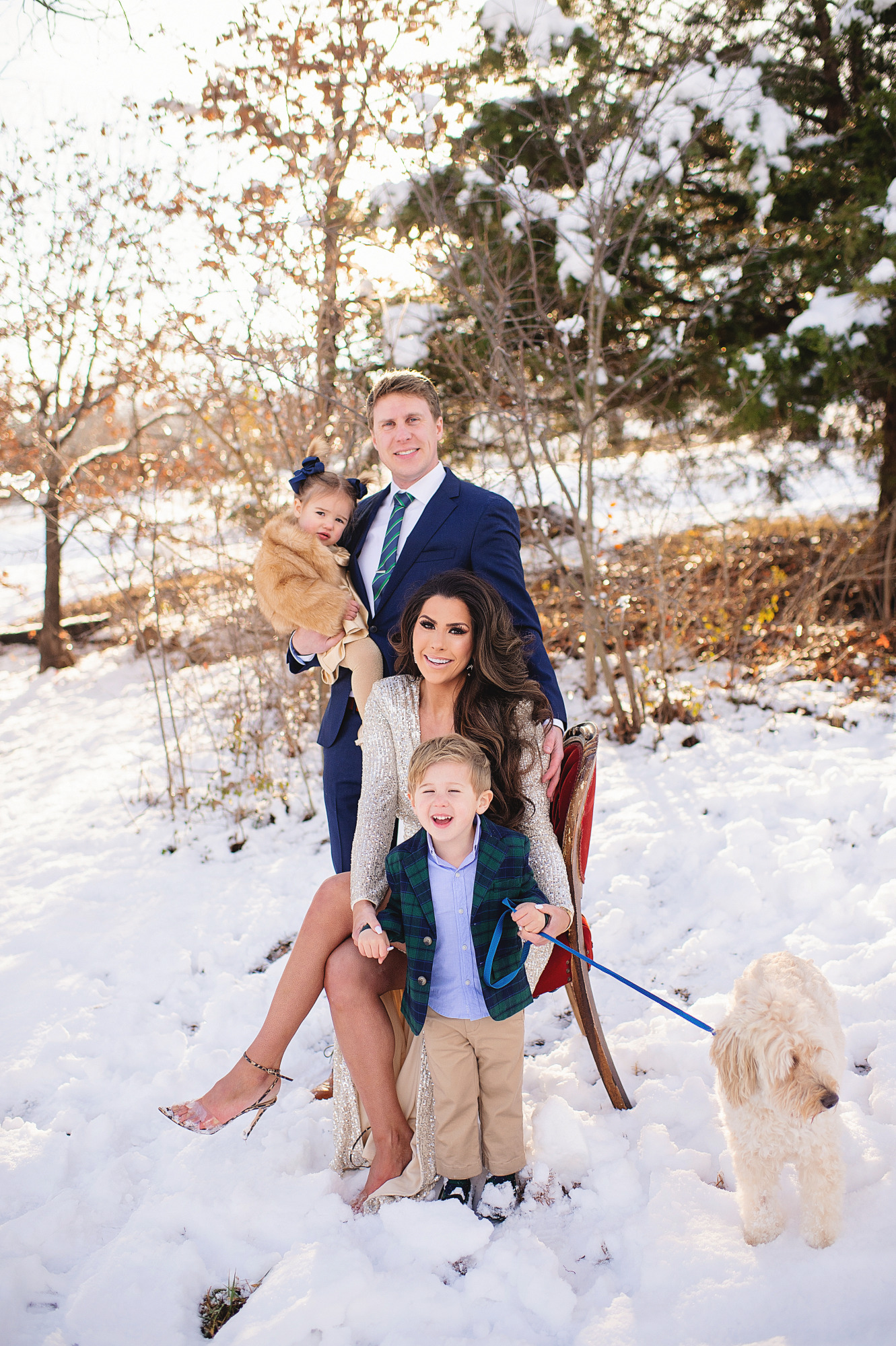 Family Christmas Card by popular US lifestyle blog, The Sweetest Thing: image of a family standing together in the snow with their dog and wearing a Eliza J sequin dress, blue suit, blue and green plaid blazer and tan pants, and a faux fur coat and gold dress. 