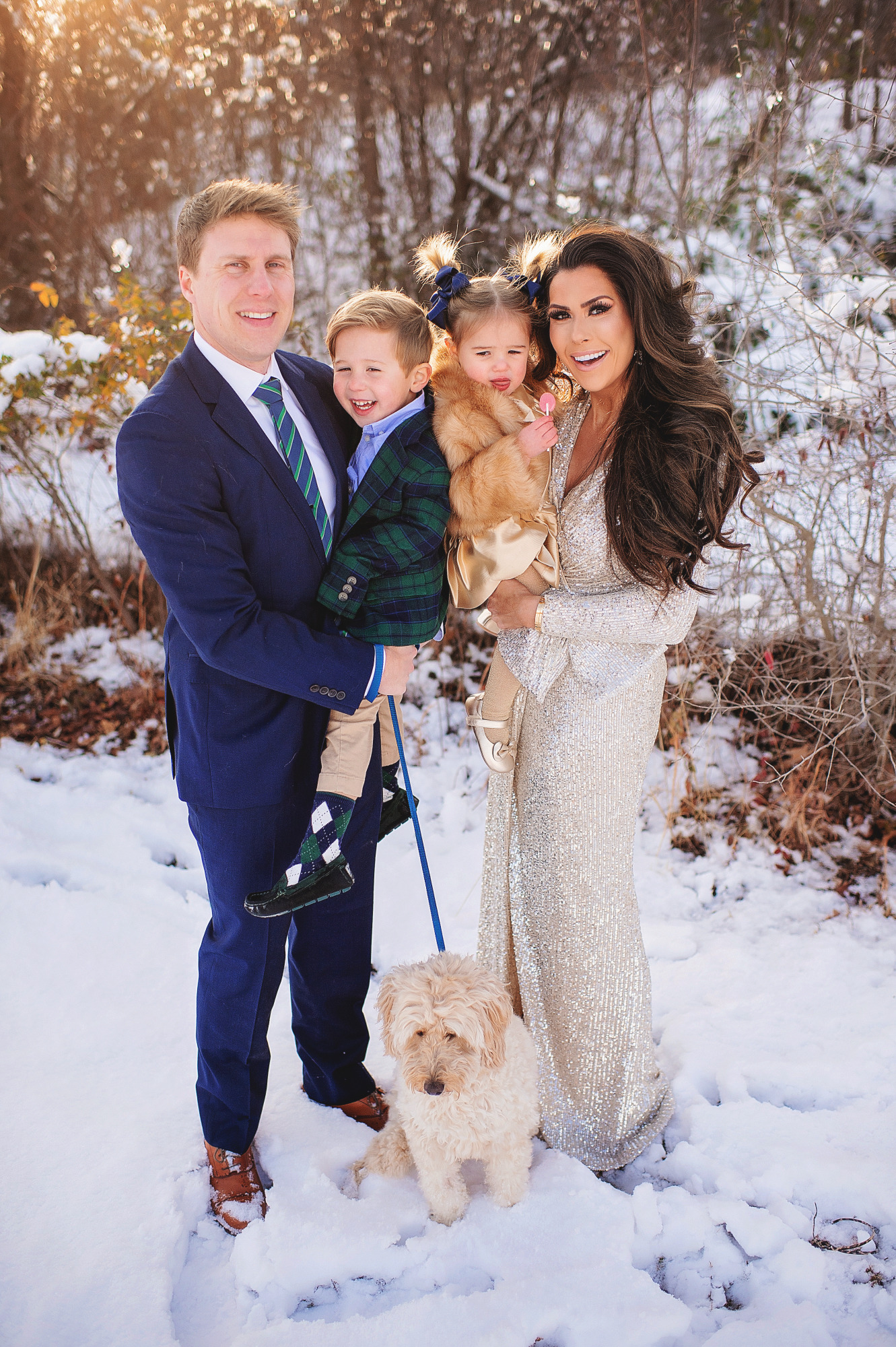 Family Christmas Card by popular US lifestyle blog, The Sweetest Thing: image of a family standing together in the snow with their dog and wearing a Eliza J sequin dress, blue suit, blue and green plaid blazer and tan pants, and a faux fur coat and gold dress. 